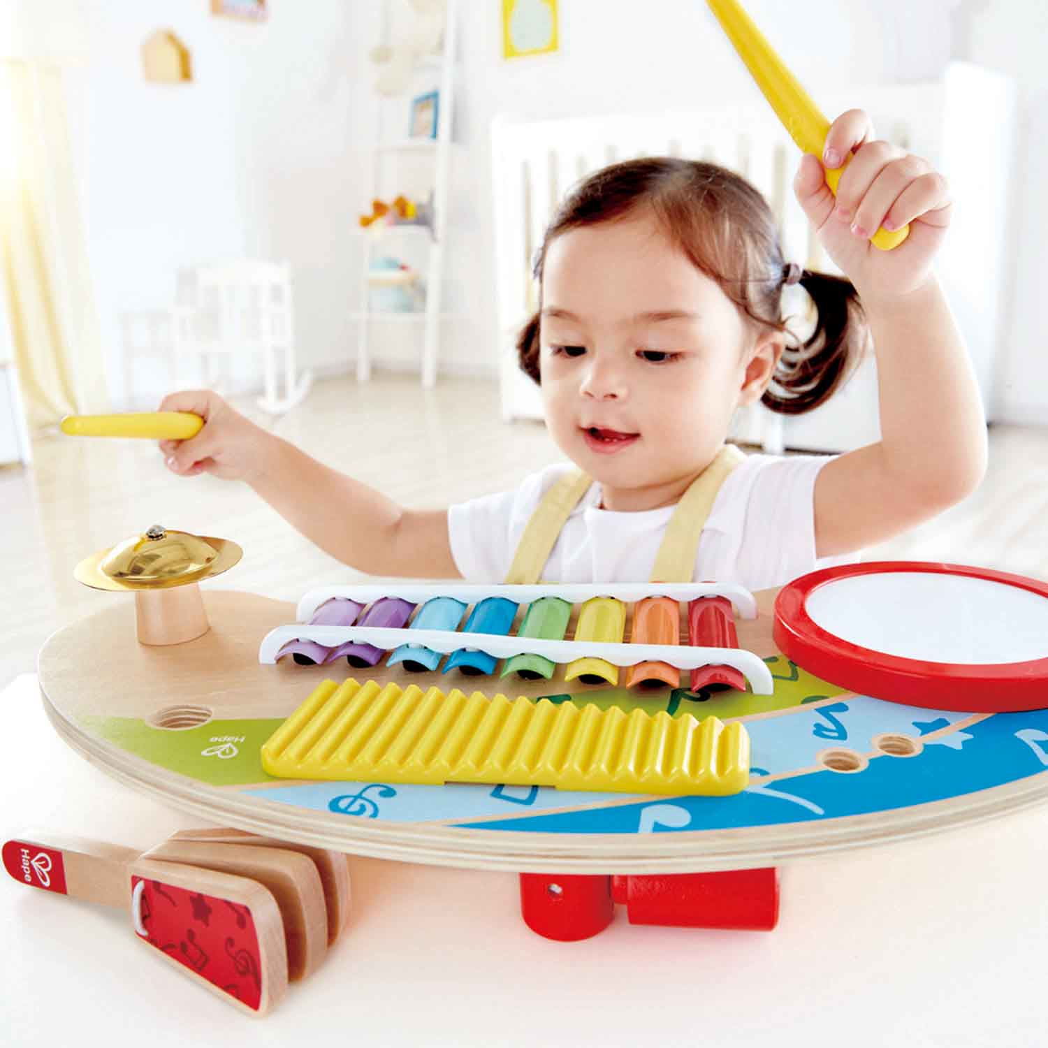 Dziecko bawiące się instrumentami muzycznymi, w tym talerzami i ksylofonem. Dziecko się uśmiecha.