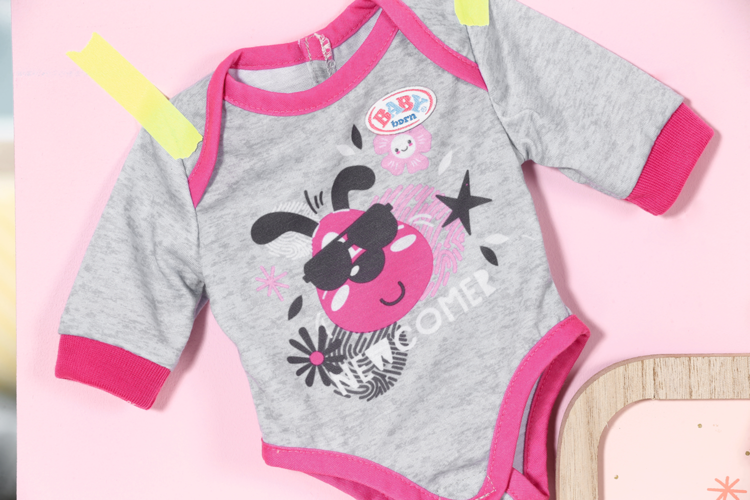 Ein Baby-Body mit Marienkäfer-Design, auf einer rosa Oberfläche befestigt. Rosa und graue Farben.