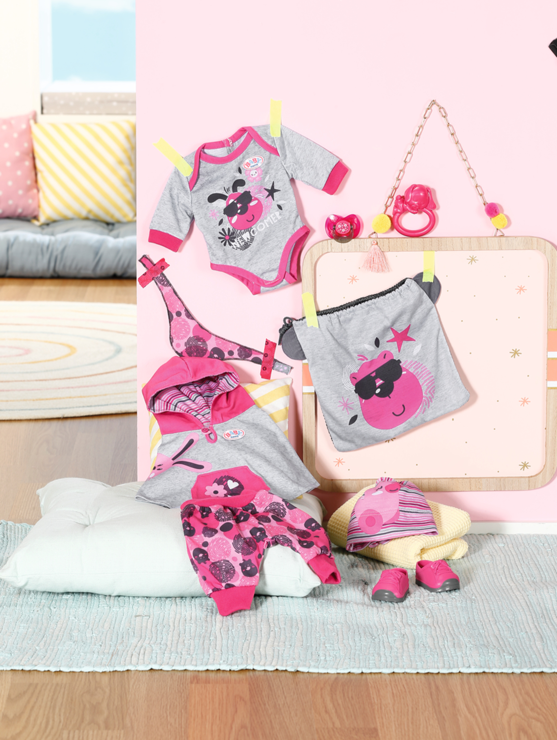 Babykleidung, darunter ein Hemd, eine Hose und ein Hut, auf rosa Hintergrund.