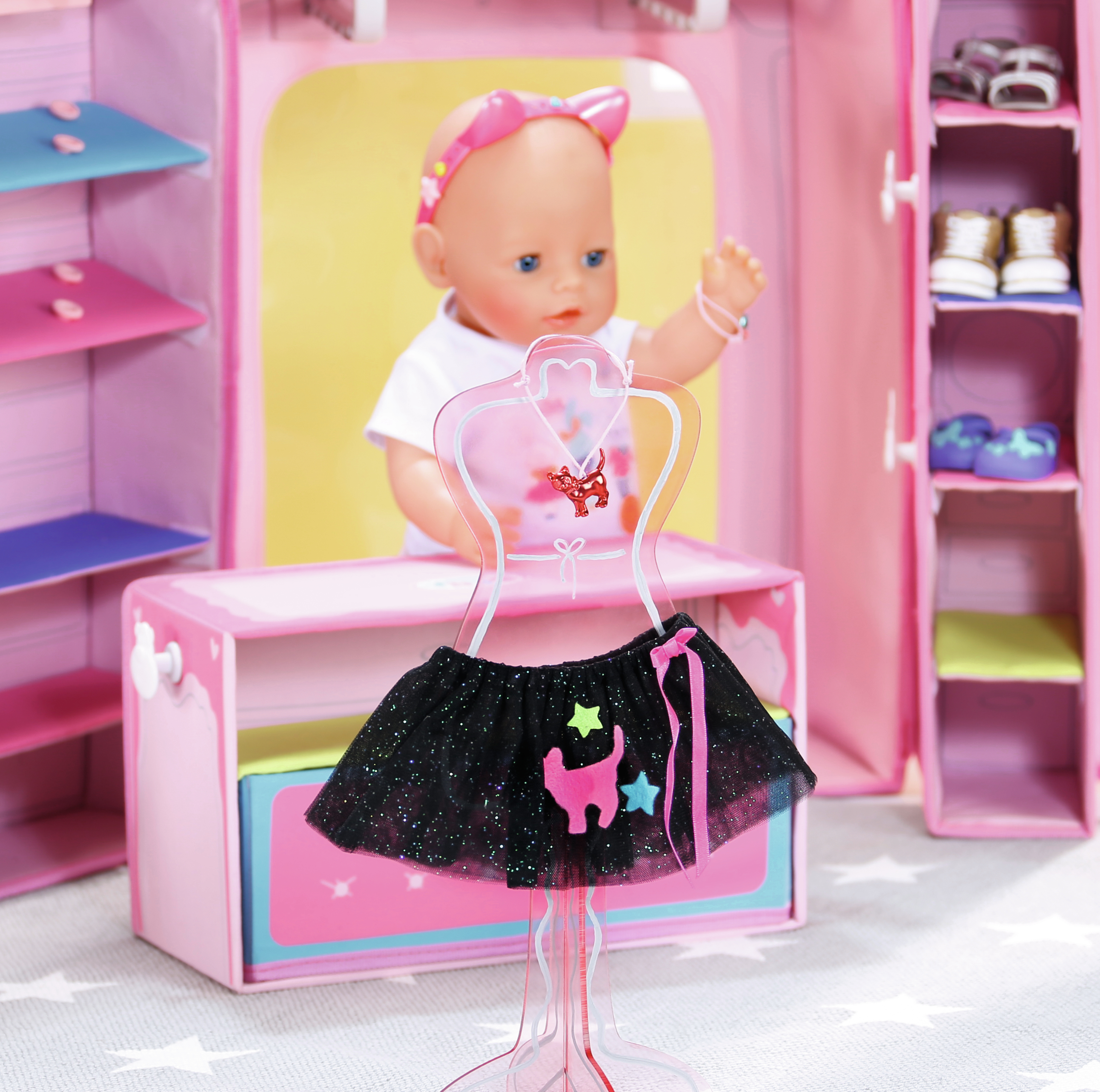 Lalka z różową opaską za manekinem z czarną spódnicą, różowa szafa.