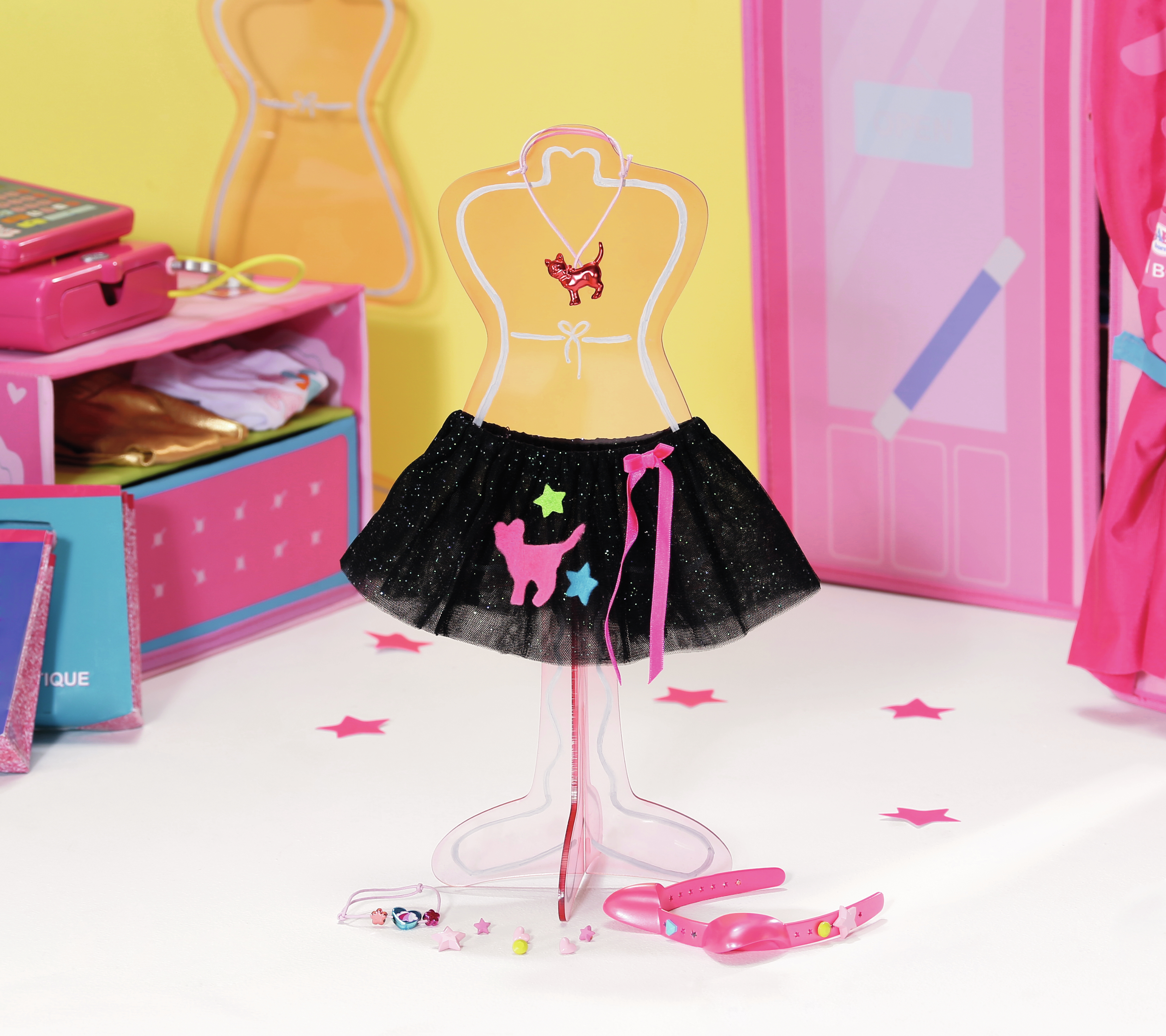 Strój dla lalki na stojaku. Ma czarną spódnicę z kształtami kota i gwiazdy. Tło to żółta ściana.