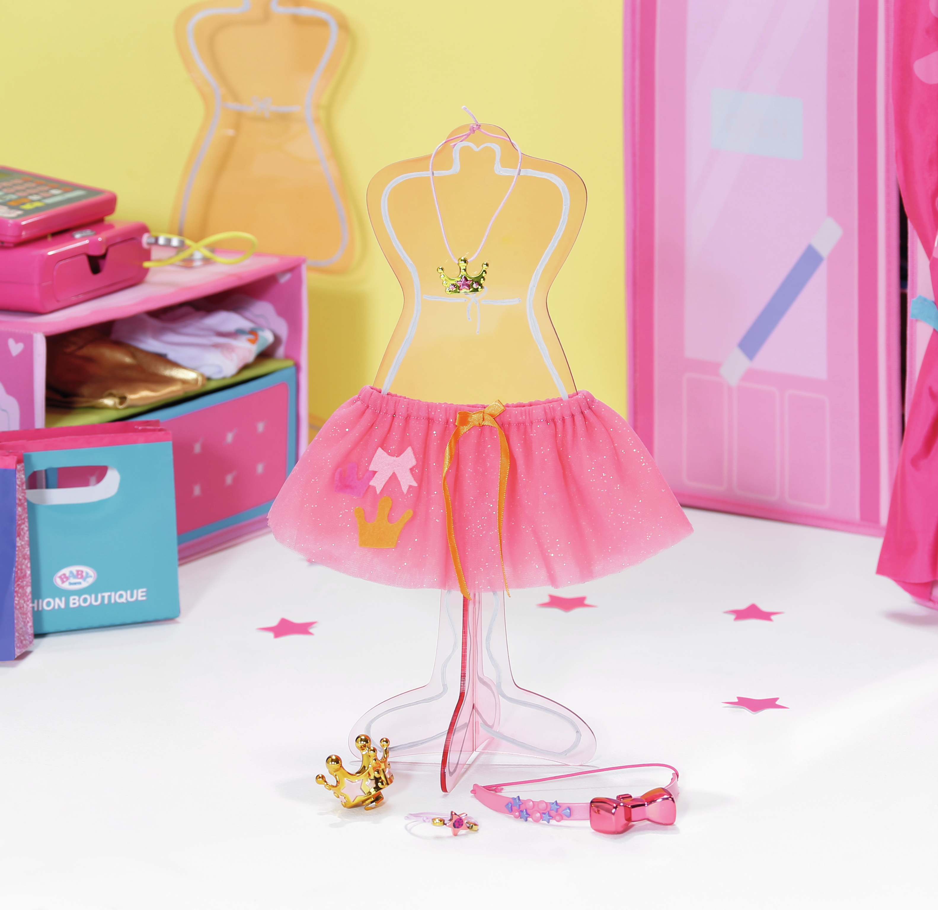 Strój dla lalki na wystawie. Strój zawiera różową tutu i koronę. Tło ma różową ścianę.