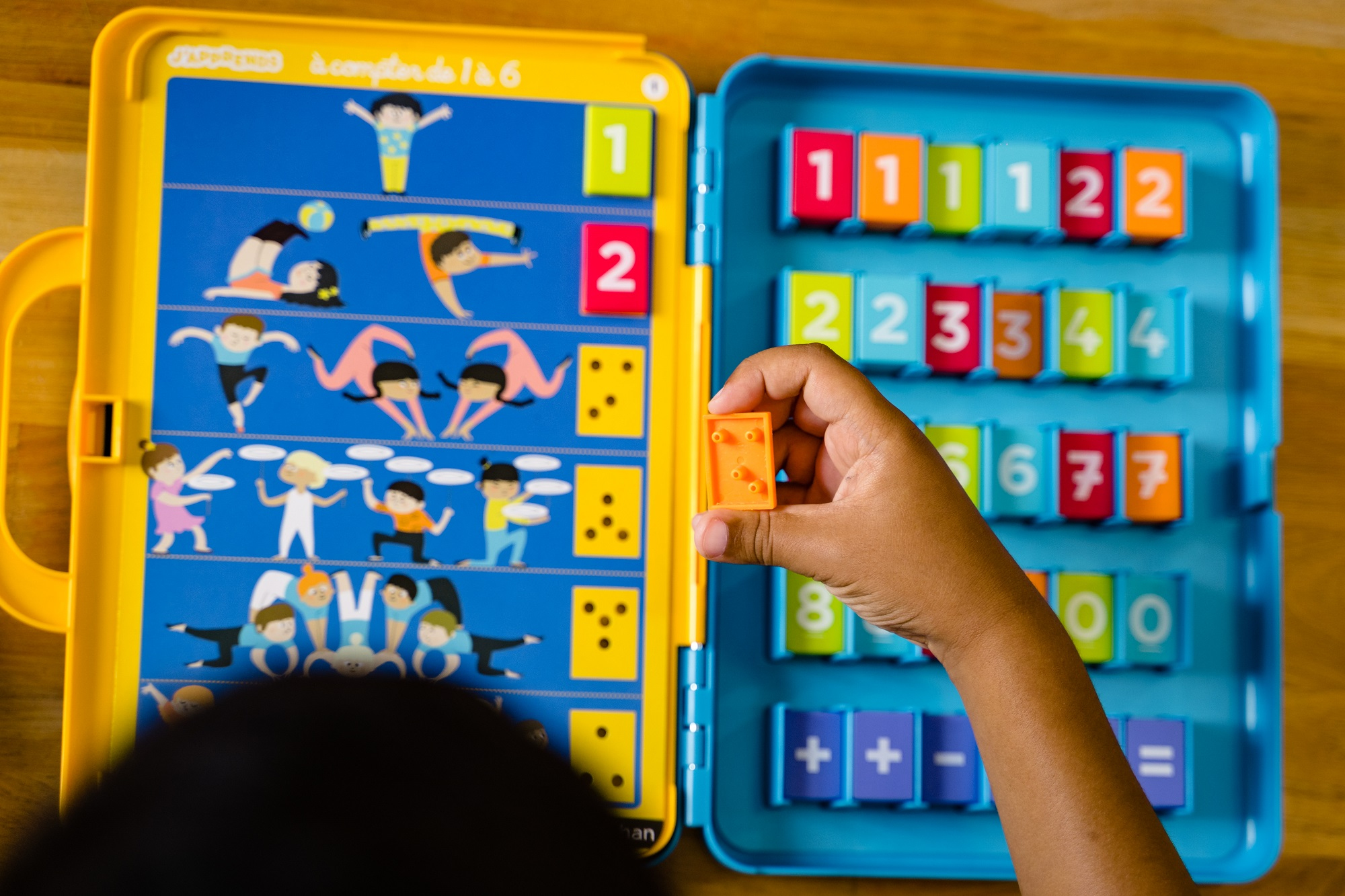 Ręka trzyma mały pomarańczowy element z kolorowej gry liczenia na stole.