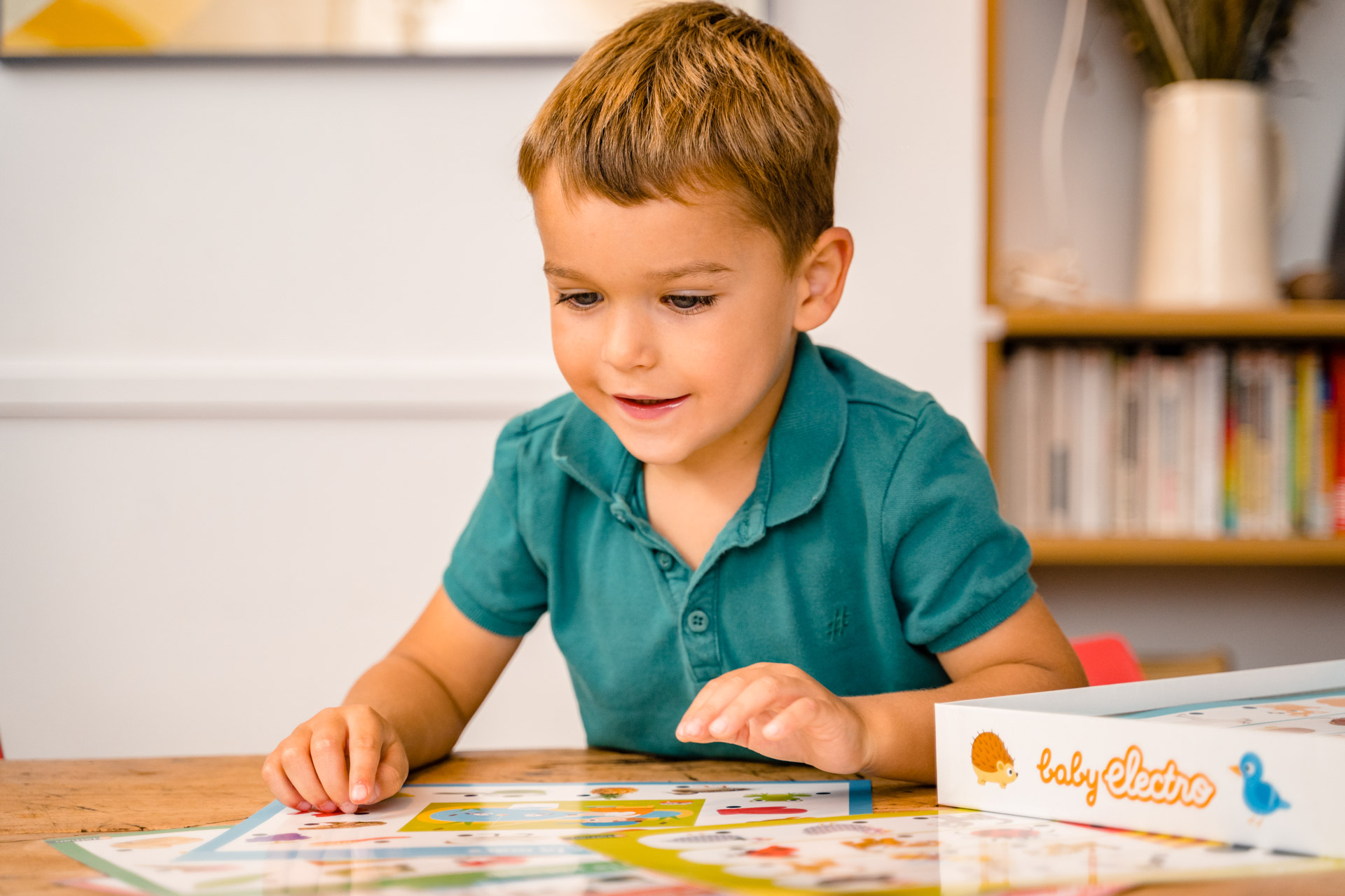 Mały chłopiec w zielonej koszuli patrzy na kolorową planszę do gry na drewnianym stole.