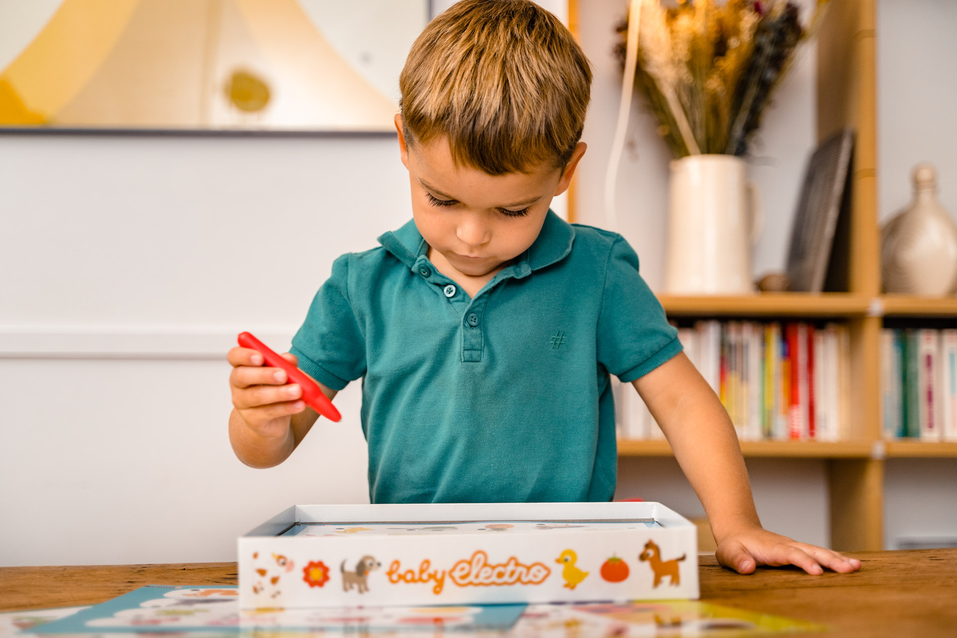 Mały chłopiec w zielonej koszuli bawiący się zabawką na stole, w pomieszczeniu.