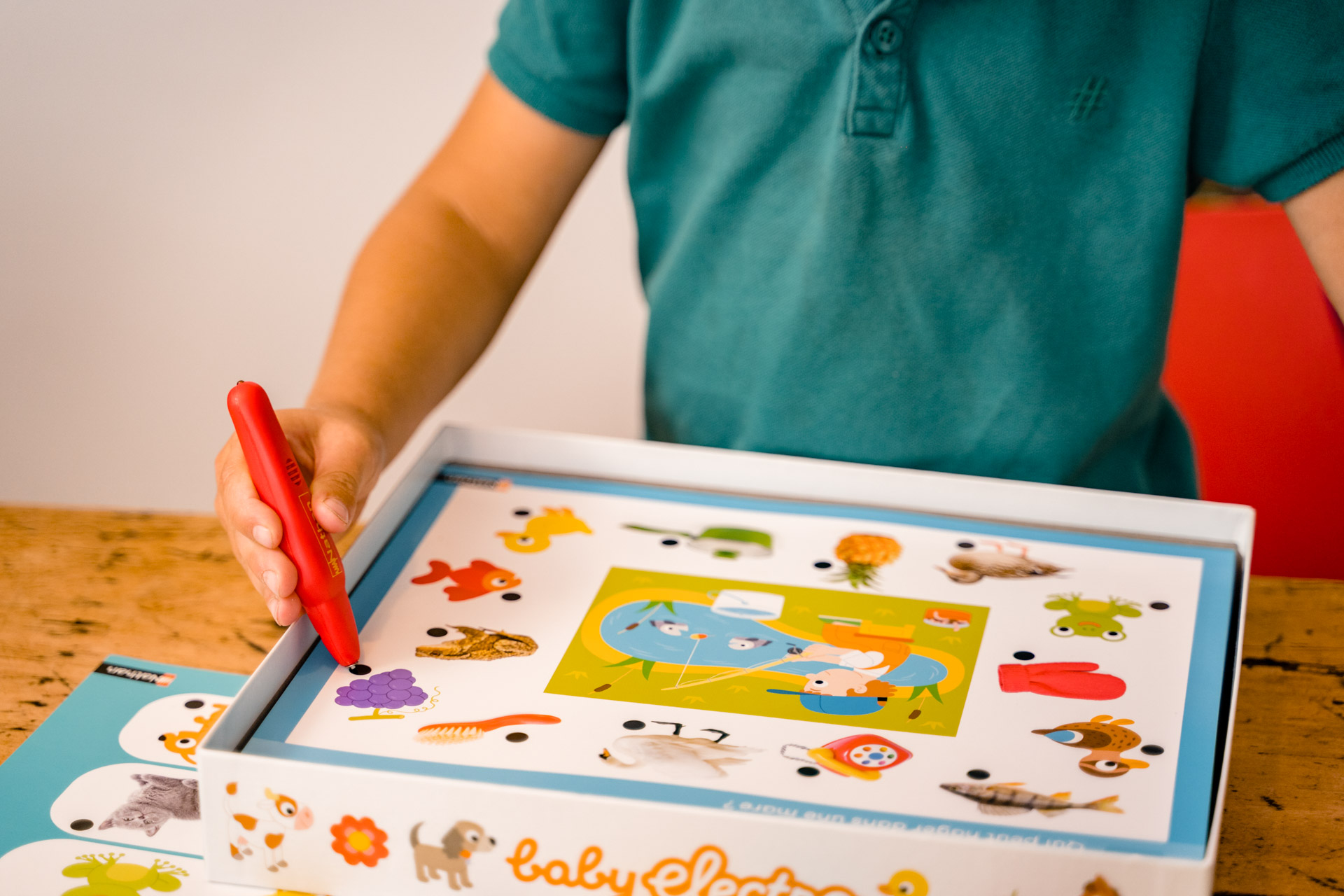 Zabawka dla dziecka i czerwony długopis na stole. W tle widoczny regał z książkami.