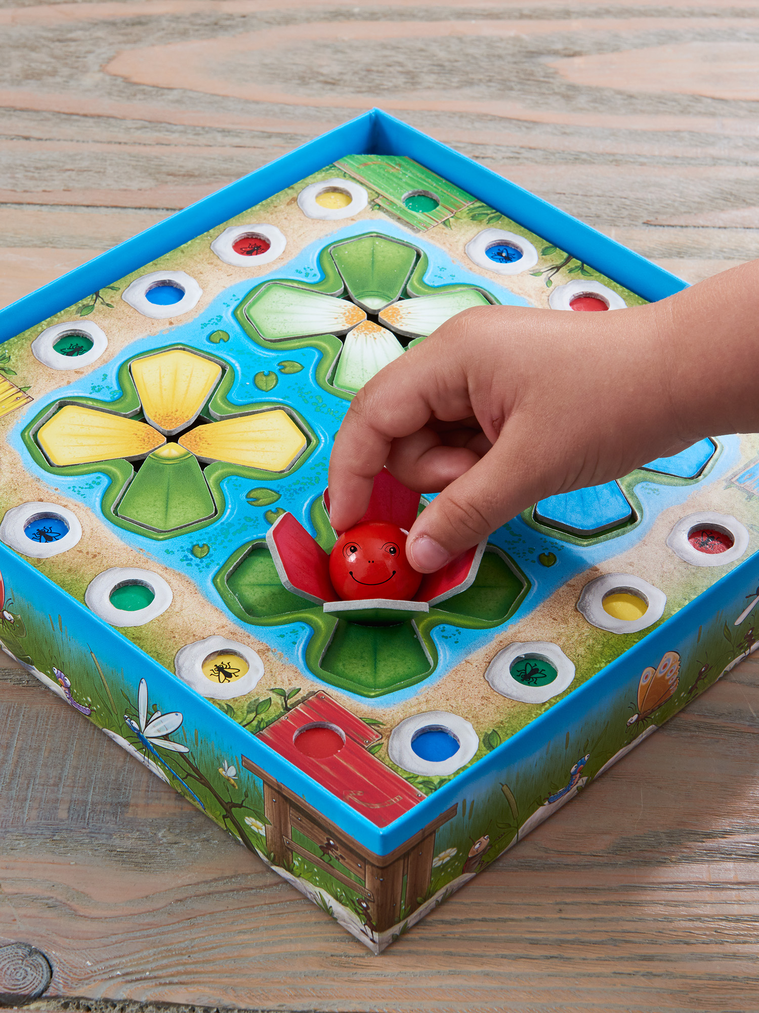 Ręka umieszczająca czerwony element biedronki na grze planszowej. Gra ma wodę i liście lilii wodnych.