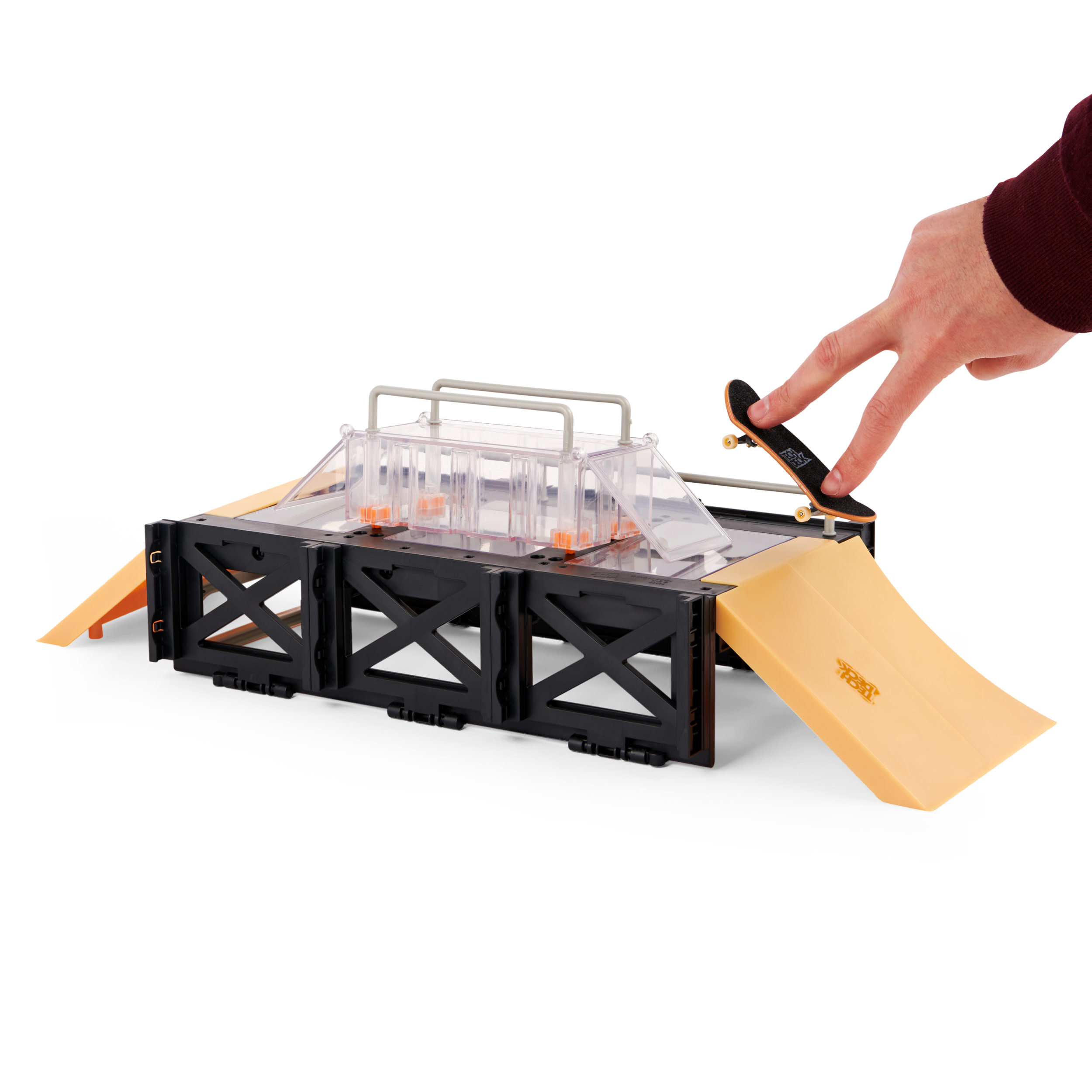 Dłoń dotyka palcem deskorolki na zestawie ramp Tech Deck. Żółty i czarny.