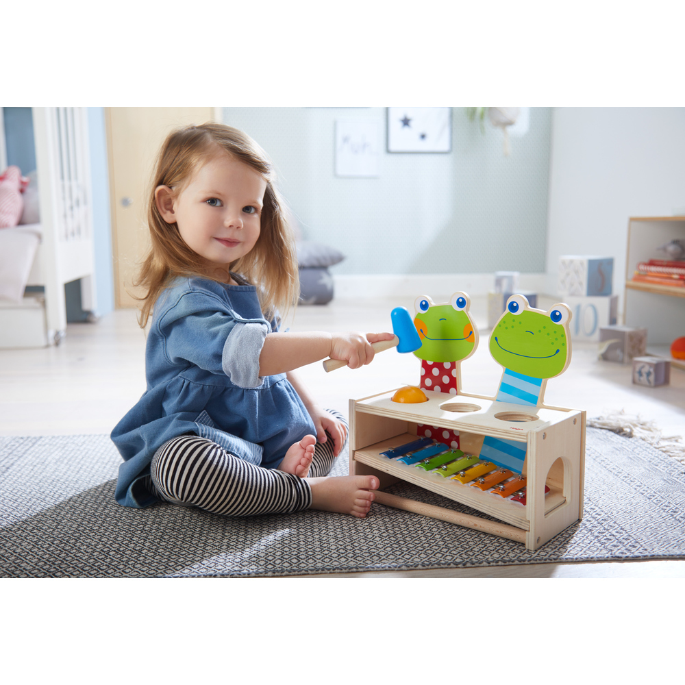 Ein junges Mädchen spielt mit einem Holzspielzeug-Xylophon und Hammer.