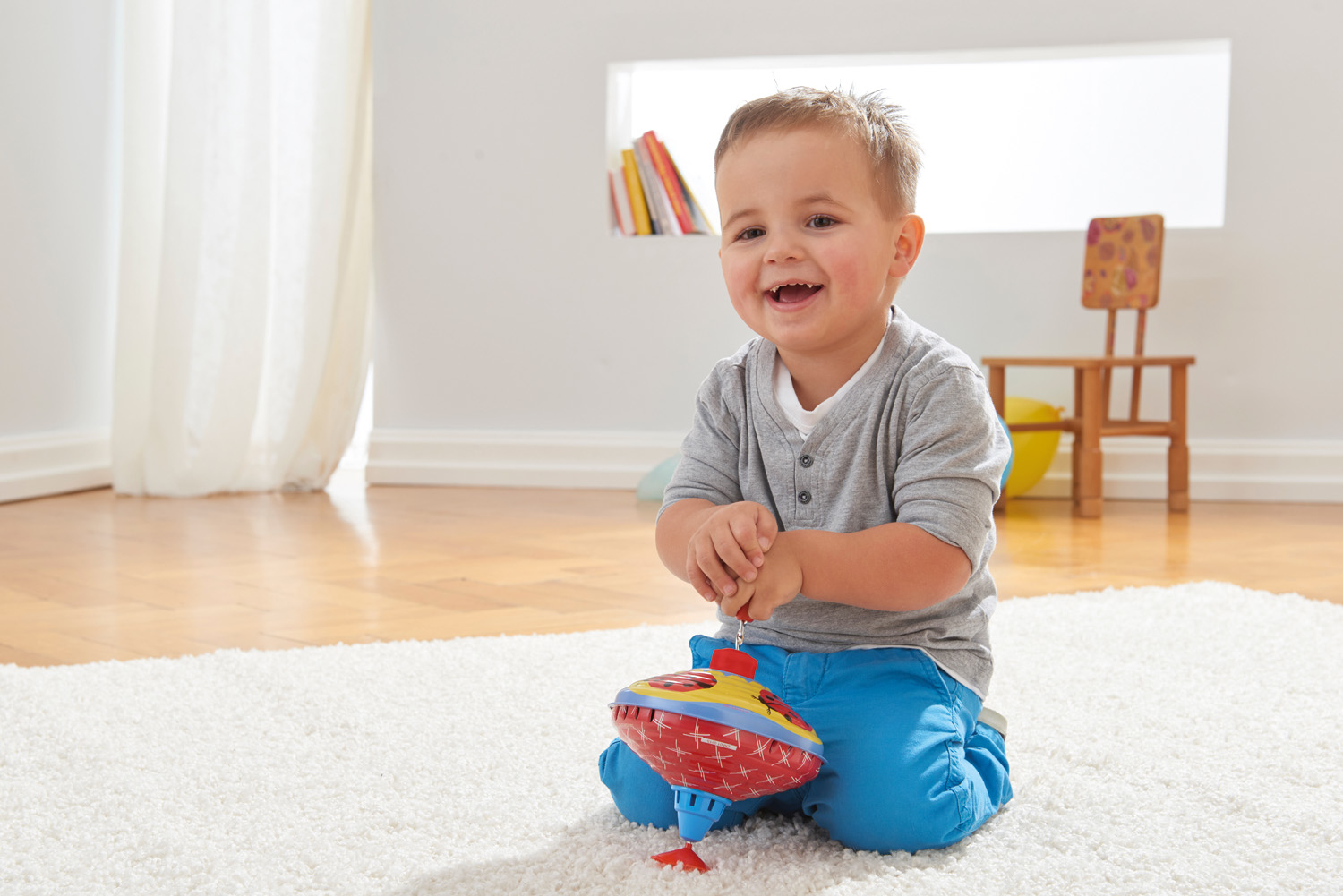 Mały chłopiec siedzi na dywanie i bawi się czerwoną i żółtą zabawką bączkiem.