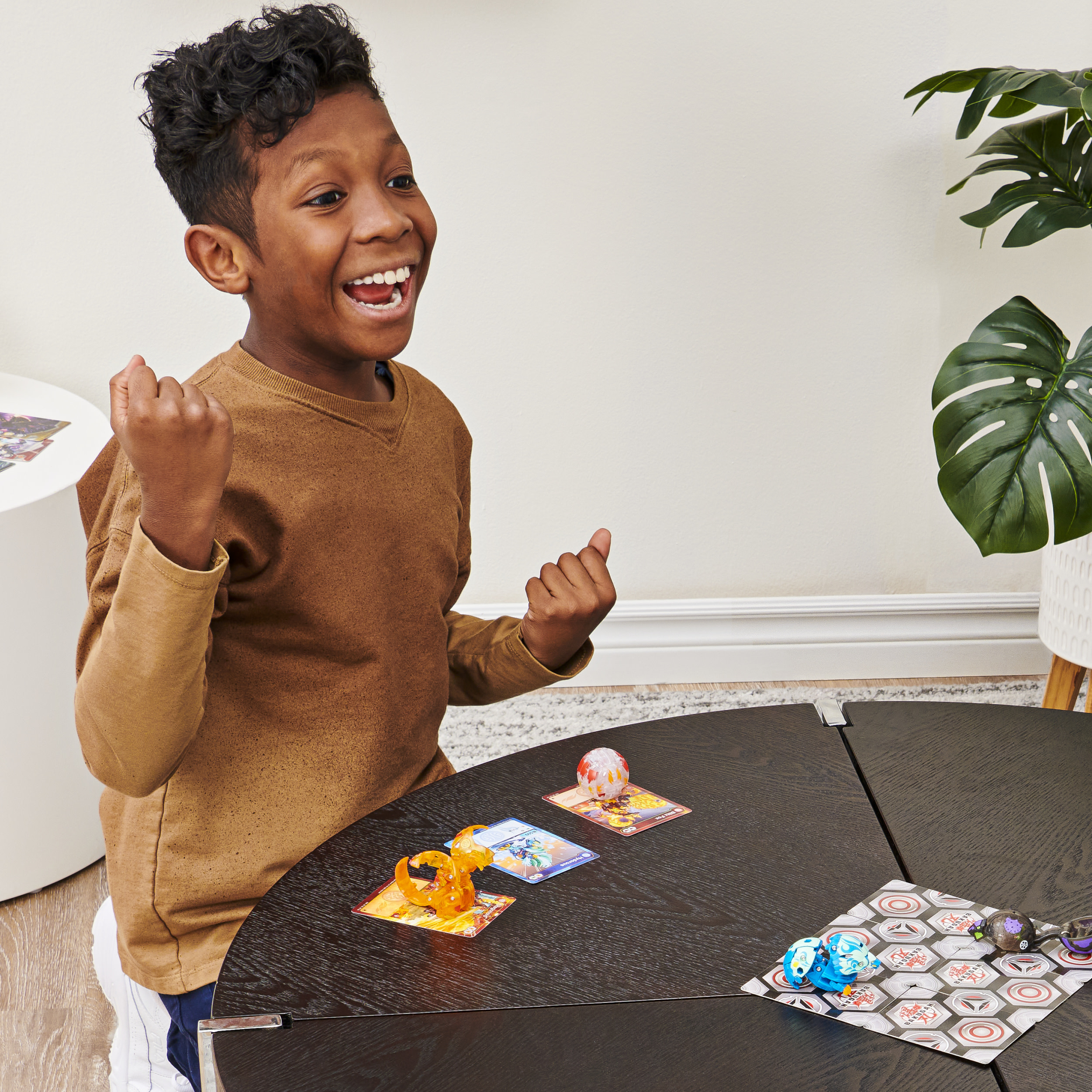 Mały chłopiec bawi się zabawkami Bakugan na stole. Uśmiecha się i jest podekscytowany.