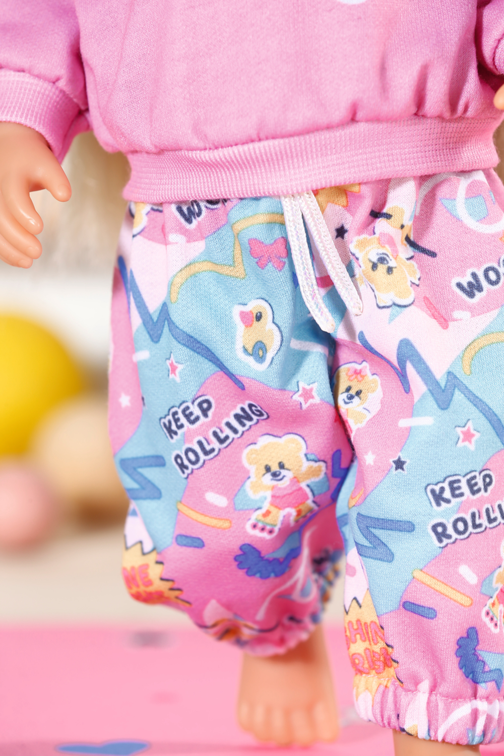 Lalka w różowych szortach z kolorowymi wzorami i napisem 'Keep Rolling'.