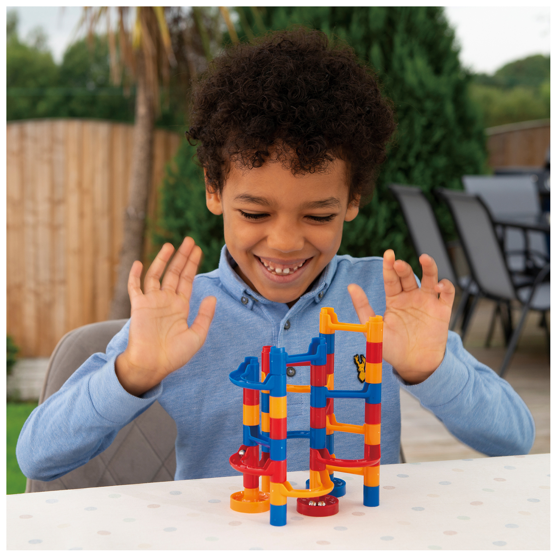 Chłopiec uśmiecha się, budując kolorową zabawkę z torem dla kulek na białym, nakrapianym stole.