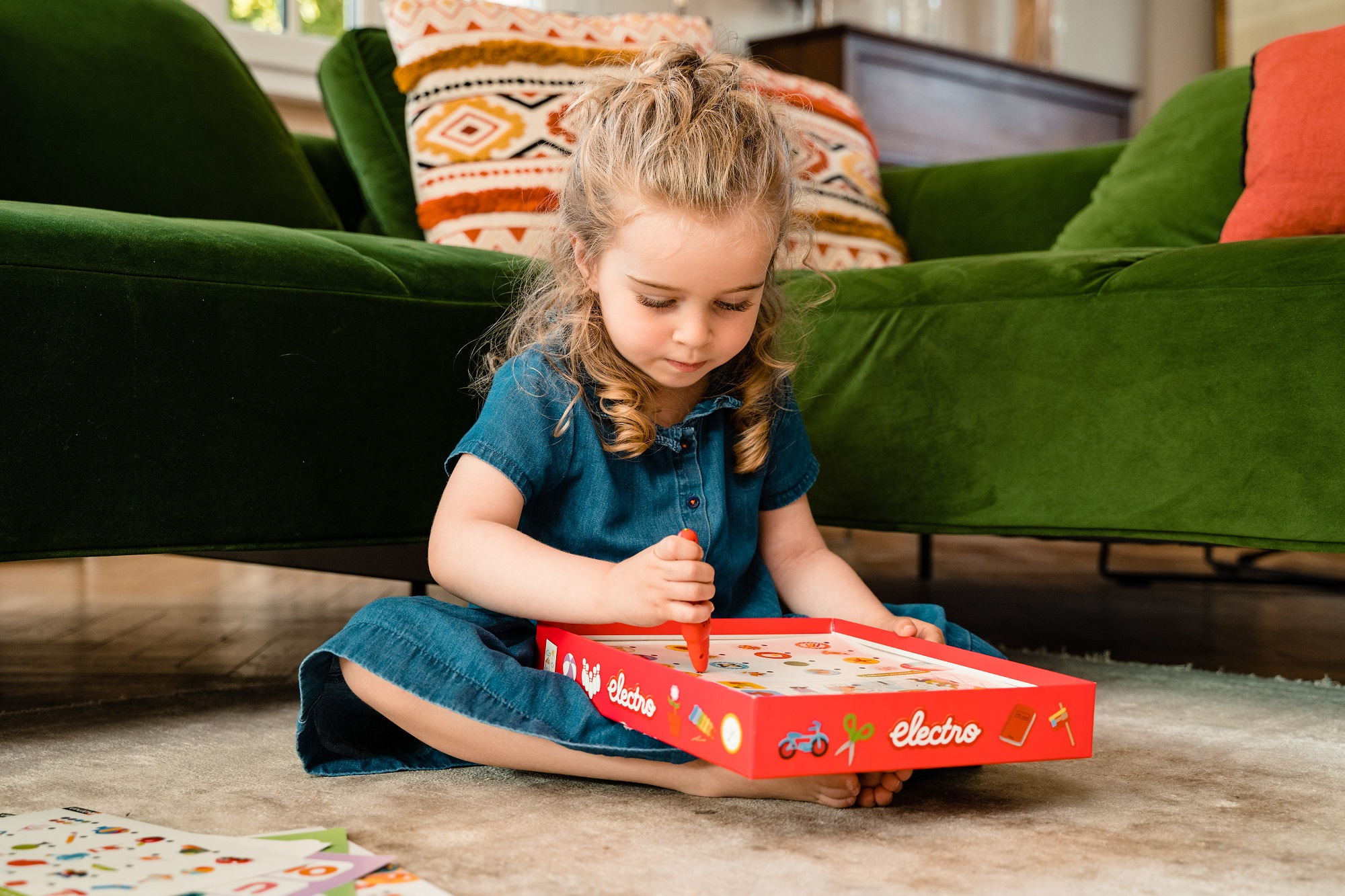 Młoda dziewczyna siedzi na podłodze, bawiąc się pudełkiem. Ma w ręku długopis.
