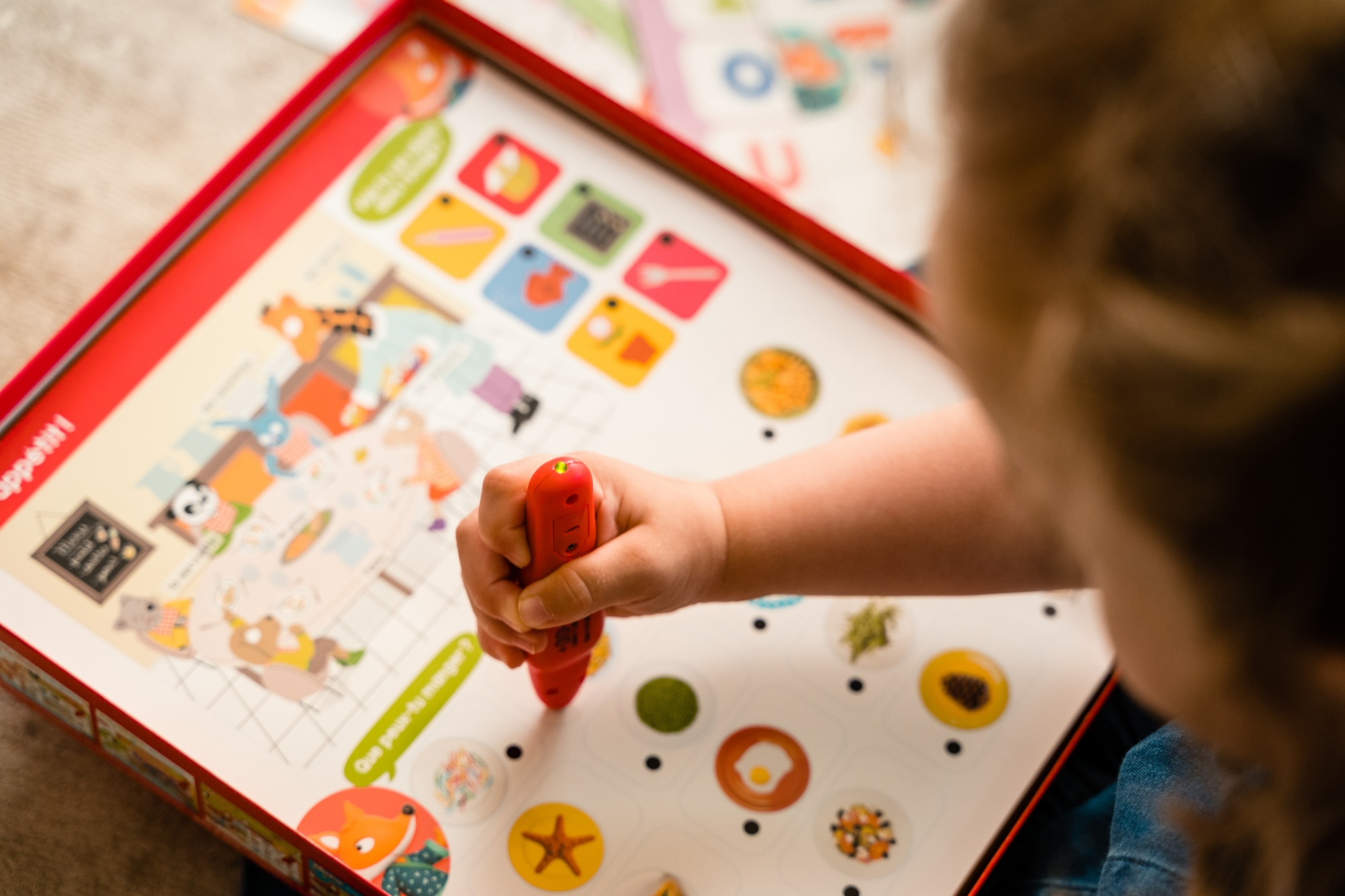 Ręka dziecka używająca czerwonego pisaka na grze planszowej z ilustracjami jedzenia.