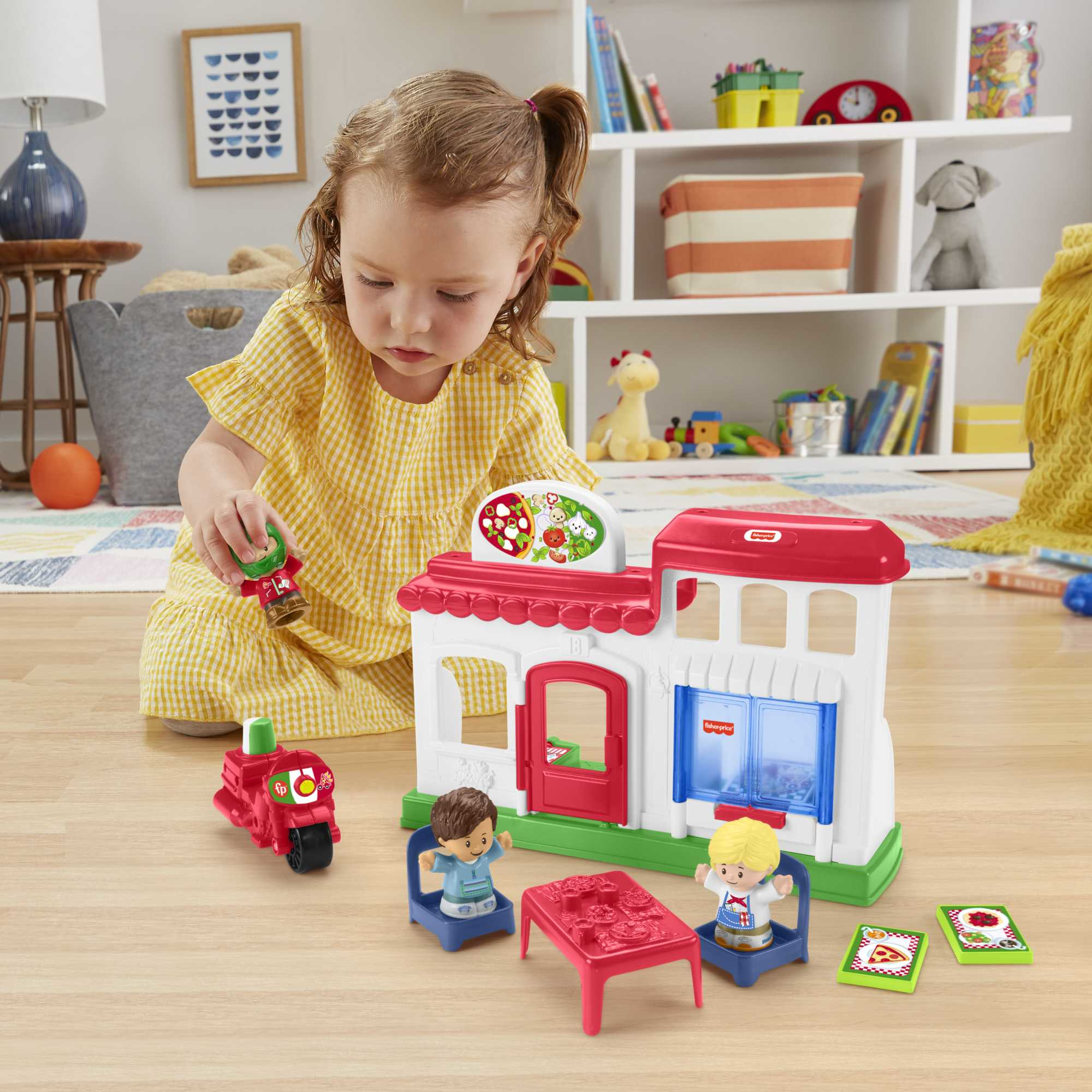 Bambina che gioca con un negozio di pizza giocattolo. Il set include un edificio, personaggi e uno scooter rosso.