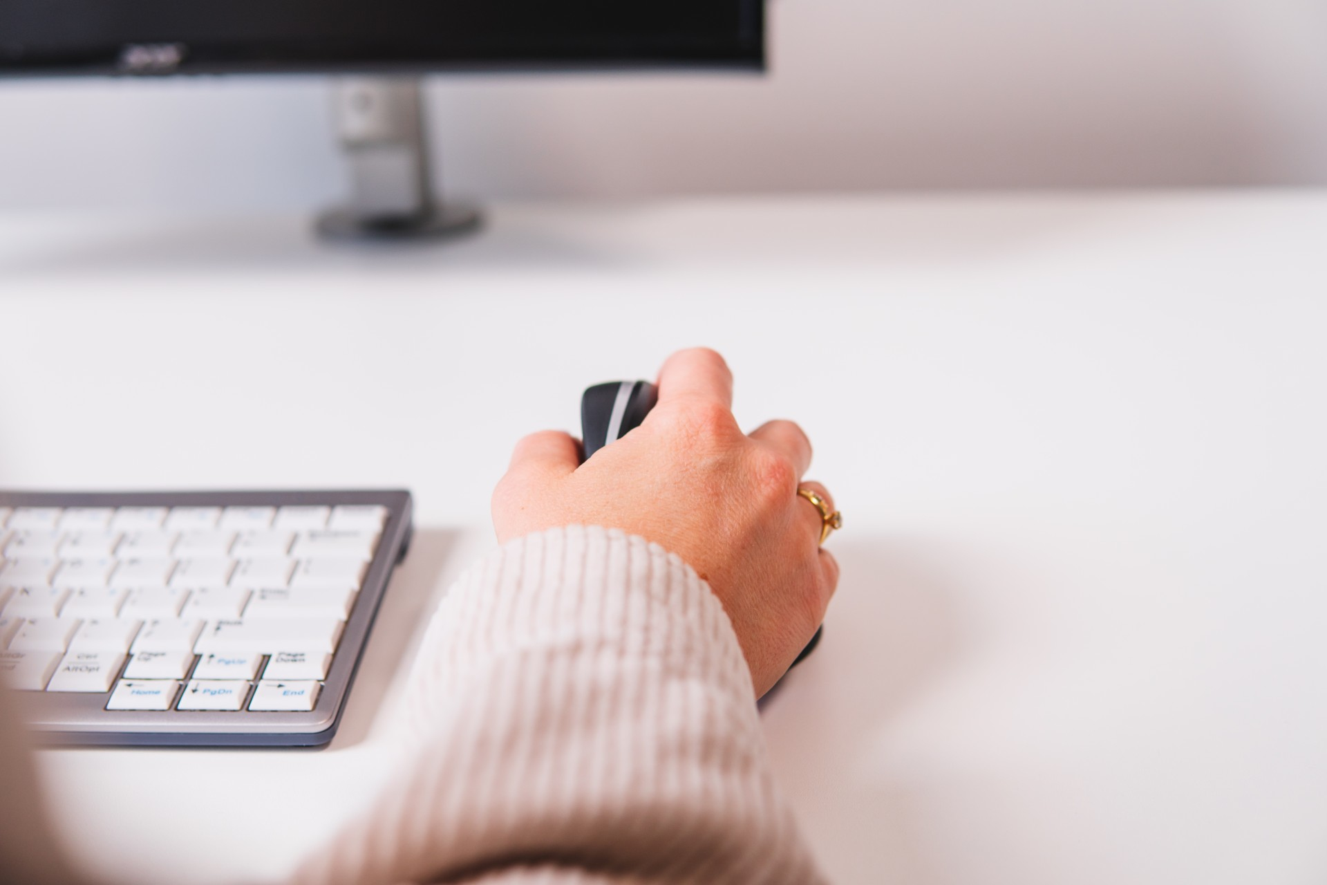 Une main utilise une souris d'ordinateur noire sur un bureau blanc. Clavier visible.