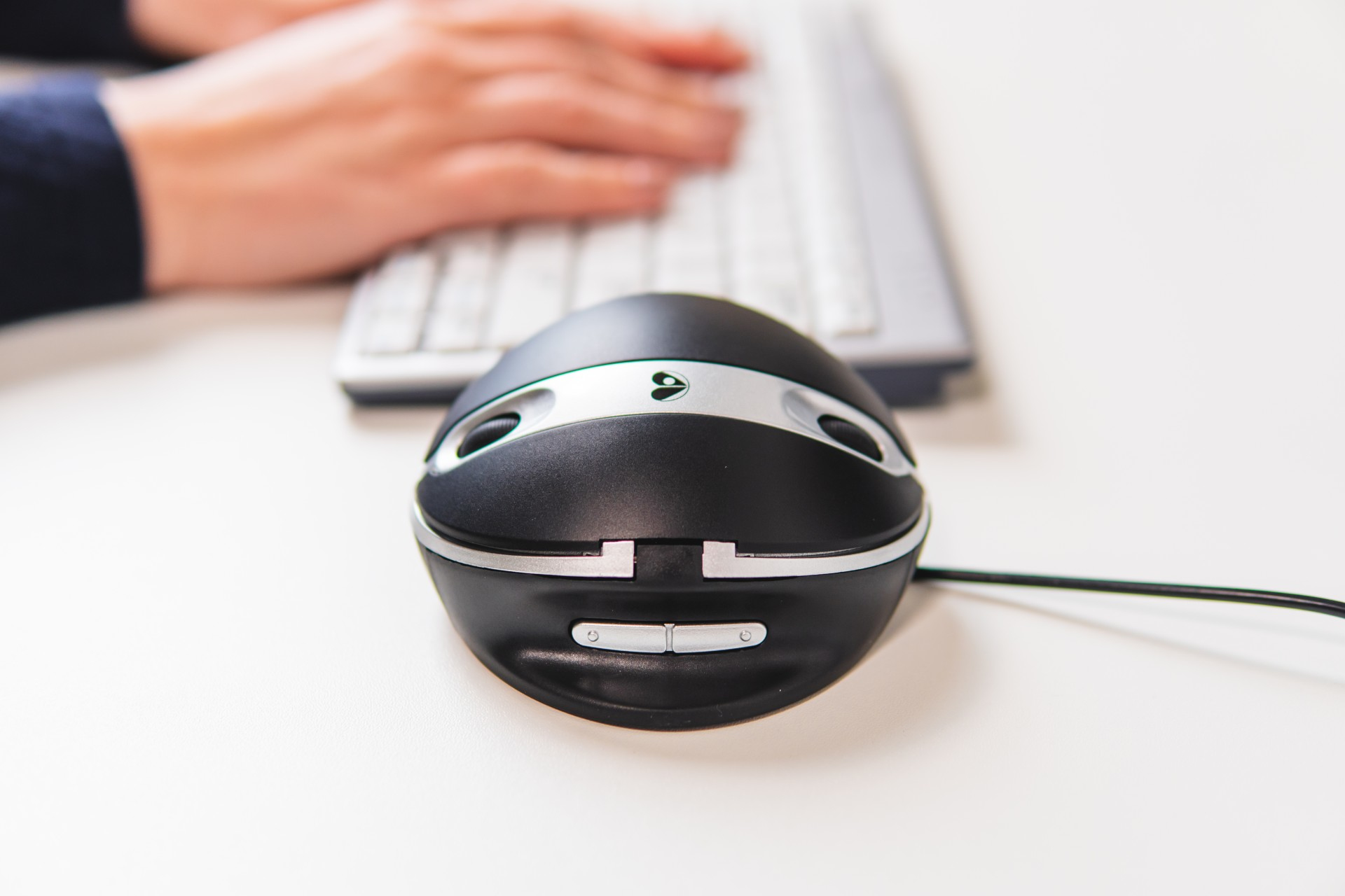Les mains d'une personne utilisant une souris d'ordinateur noire. Le clavier est visible.