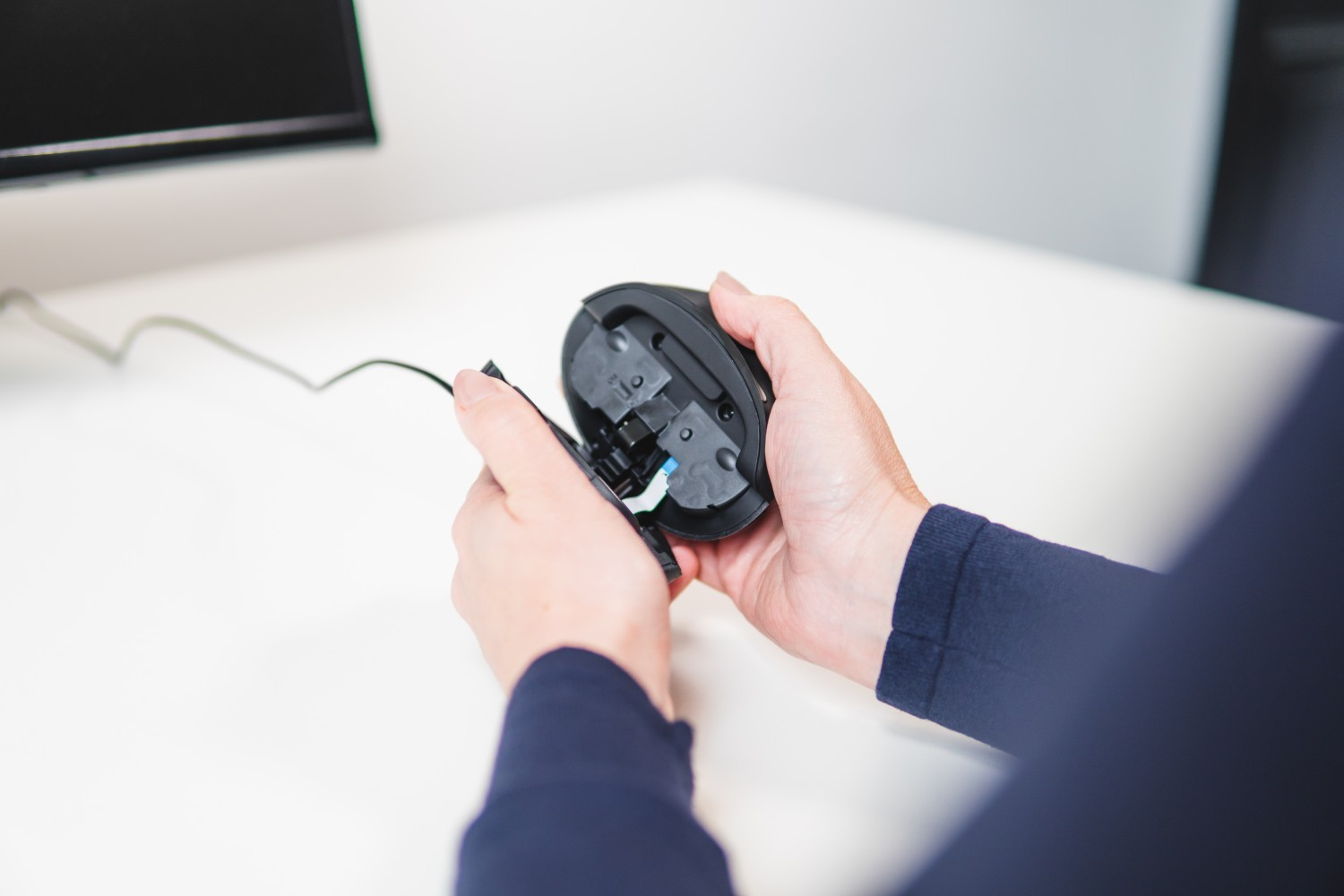 Une personne tient une souris d'ordinateur, démontée. Les composants internes sont visibles.