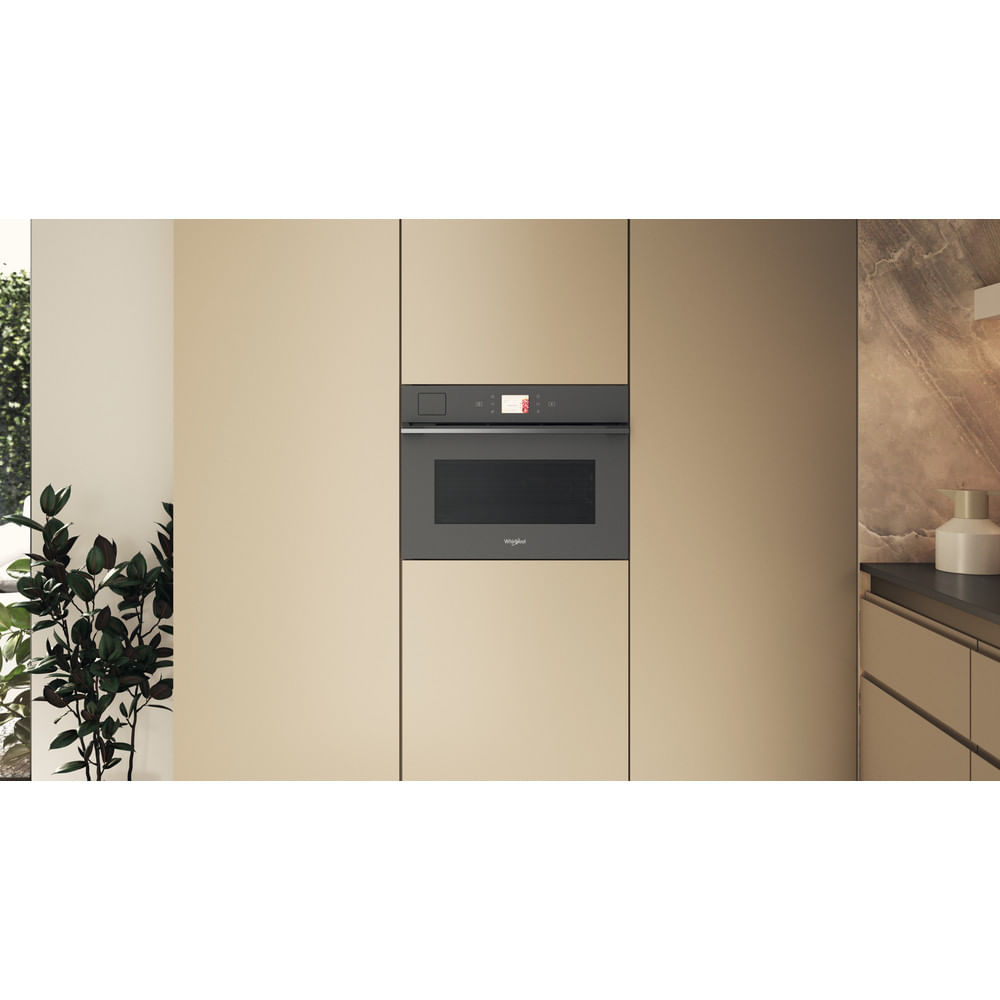Forno a microonde a incasso in un ambiente cucina. Mobili beige e pianta nella scena.