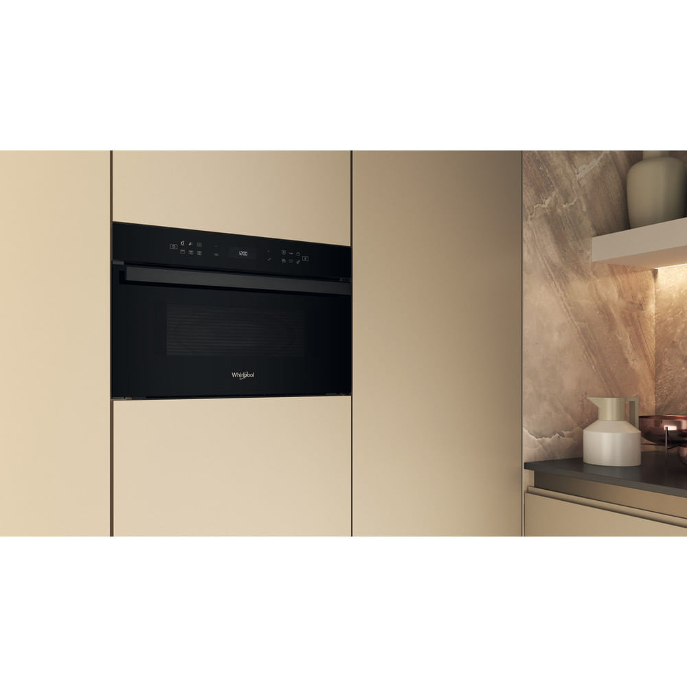 Un horno microondas negro empotrado en un armario de cocina, con pared beige y mármol.