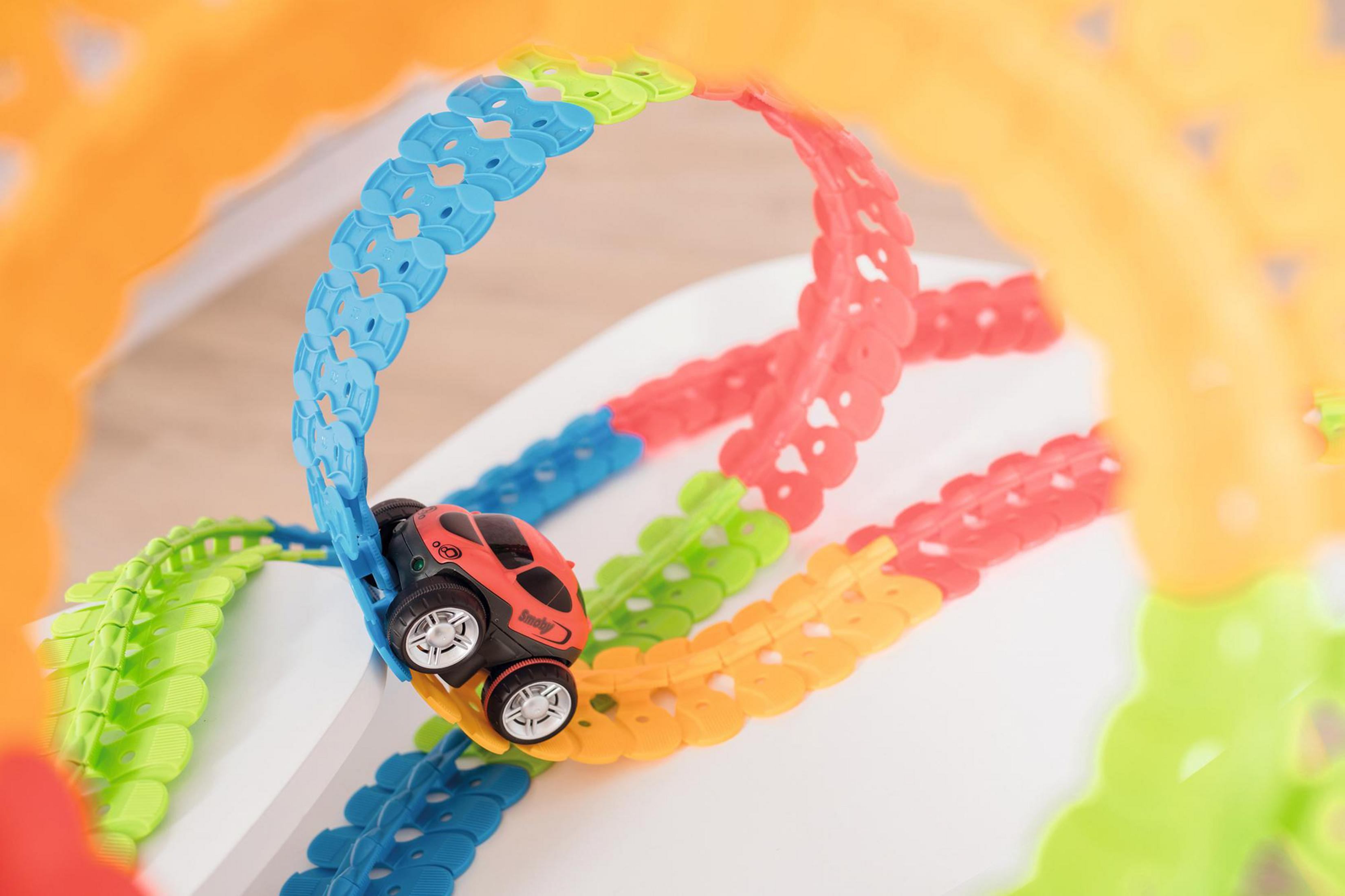 Czerwony samochodzik na kolorowym torze, z pętlami, na białej powierzchni. Rozmyte tło.