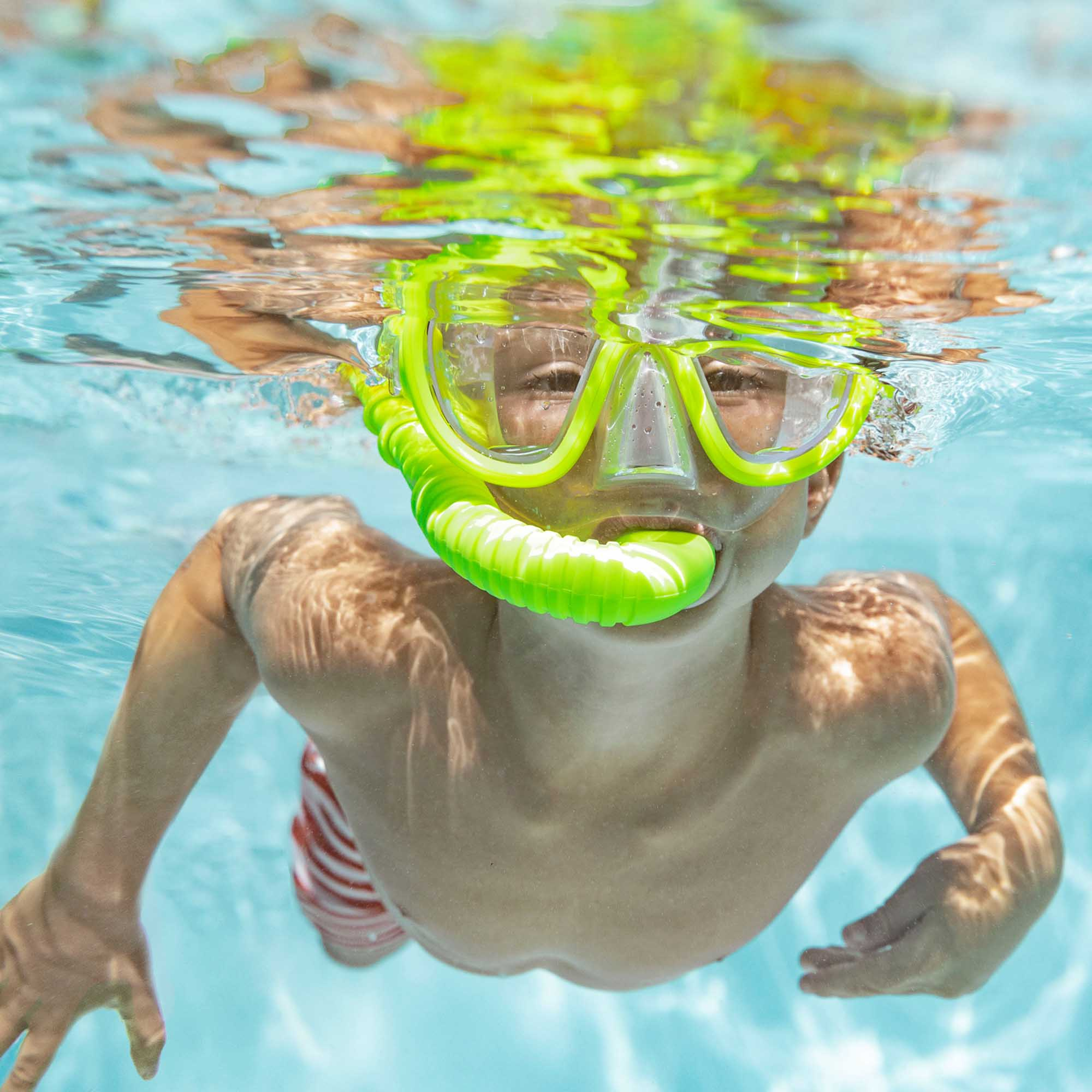 Un ragazzo in piscina con boccaglio e maschera. Il suo viso è visibile e guarda la fotocamera.