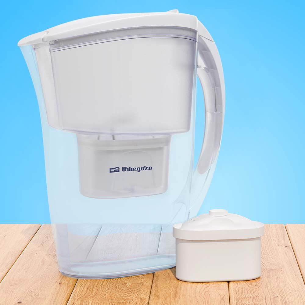 Dzbanek filtrujący wodę z oddzielnym filtrem. Przezroczysty korpus, biała pokrywa, drewniany stół i niebieskie tło.