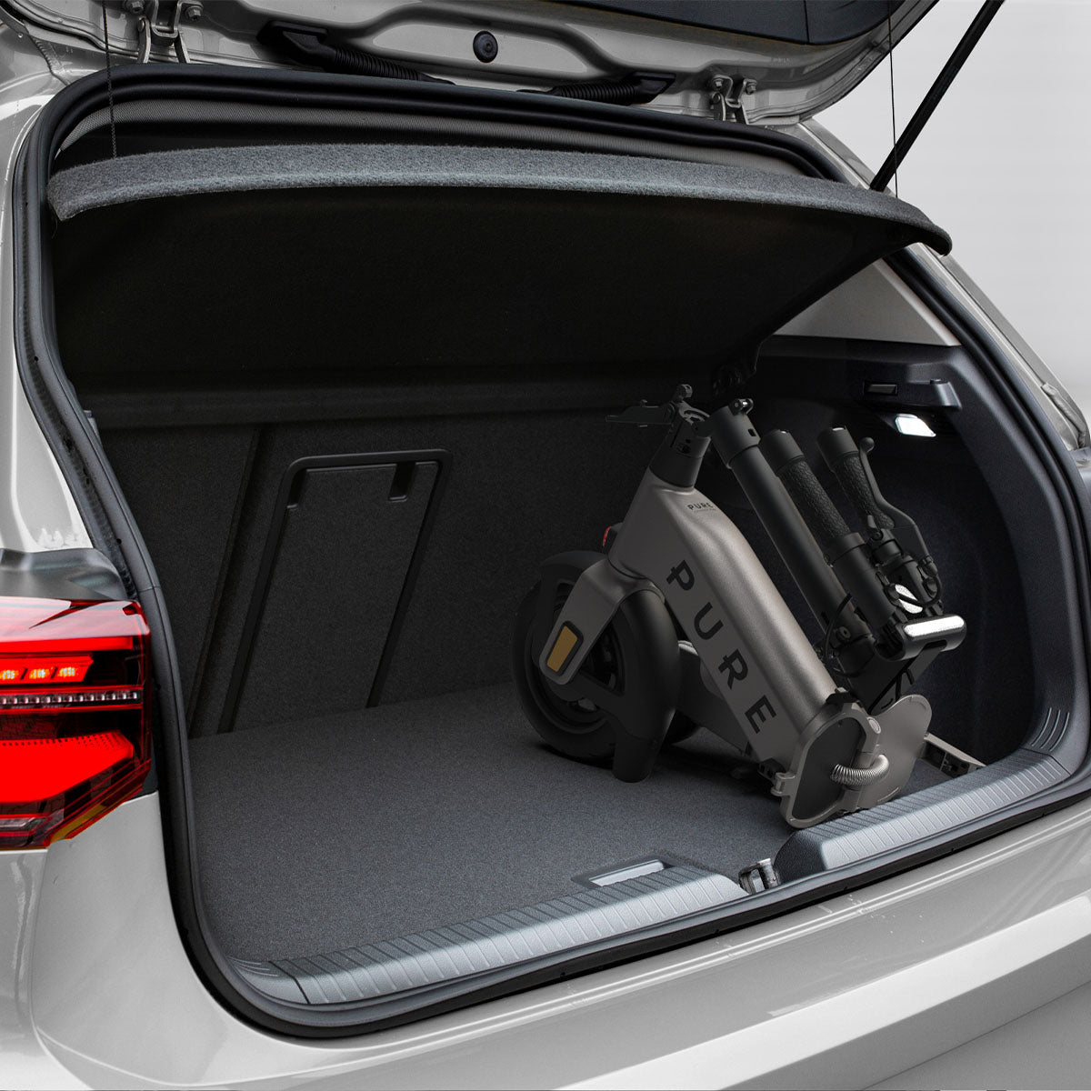 Złożona szara hulajnoga elektryczna w bagażniku samochodu. Bagażnik ma ciemnoszarą wykładzinę.