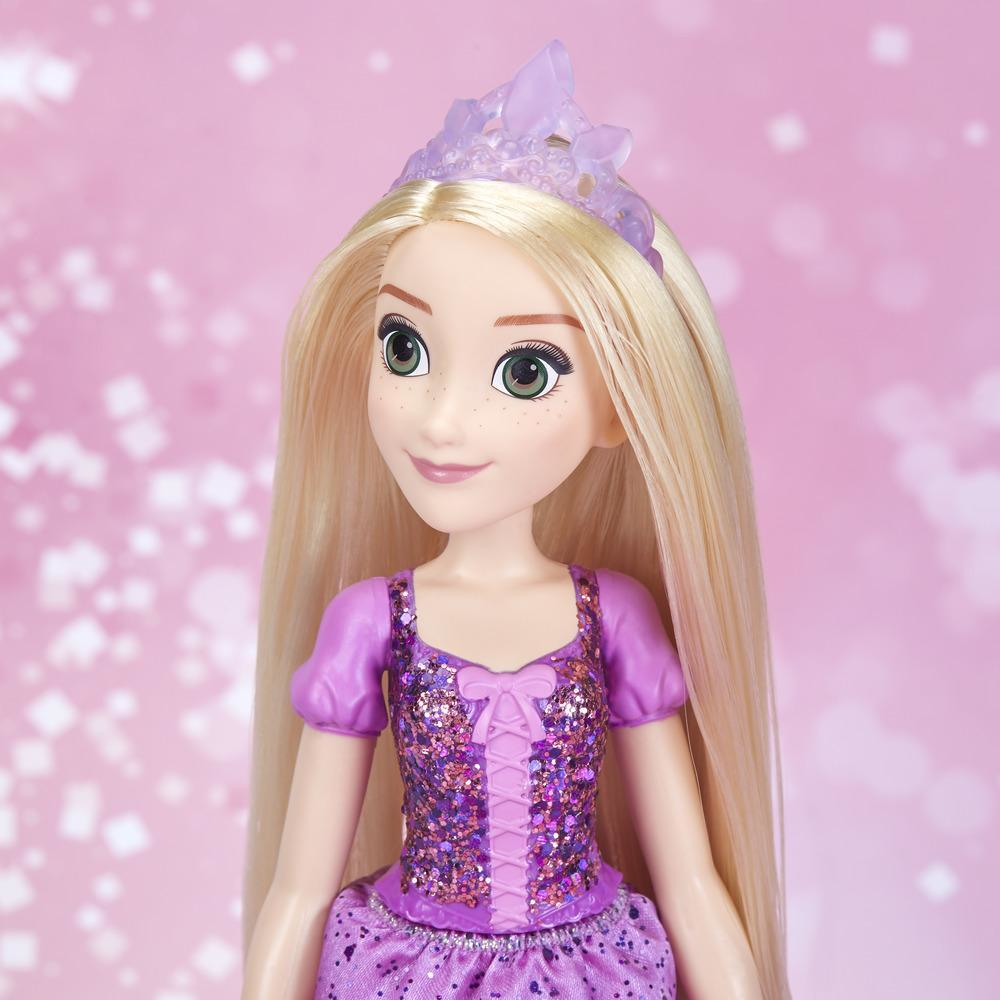 Bambola di Rapunzel. Capelli biondi, vestito viola, lentiggini e una corona. Sfondo glitterato rosa.