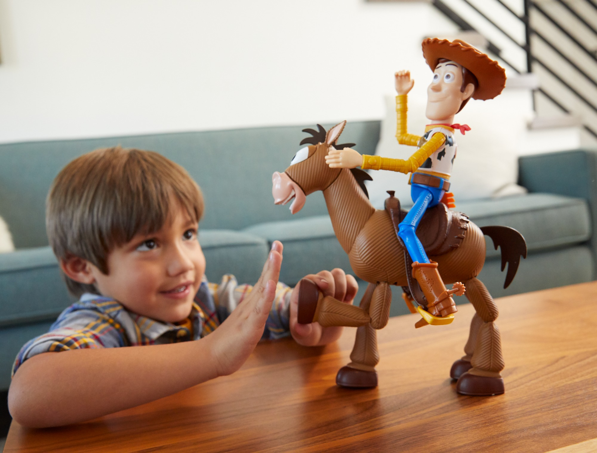 Chłopiec sięga po zabawkę Woody'ego jadącą na koniu zabawce. Zabawka jest na drewnianym stole.