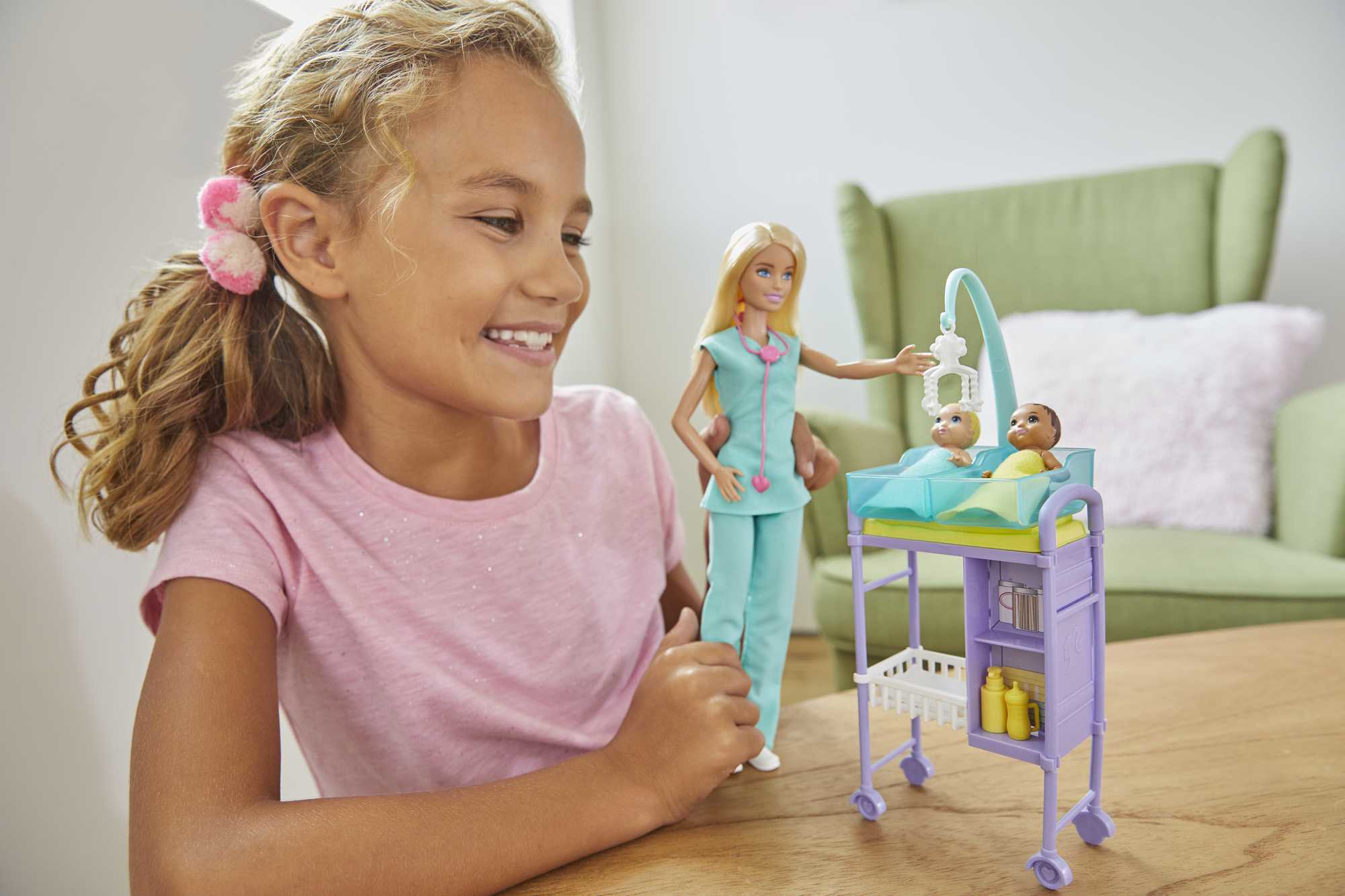 Ein Mädchen lächelt, während sie mit einer Barbie-Puppe und einem Babypflegeset spielt.