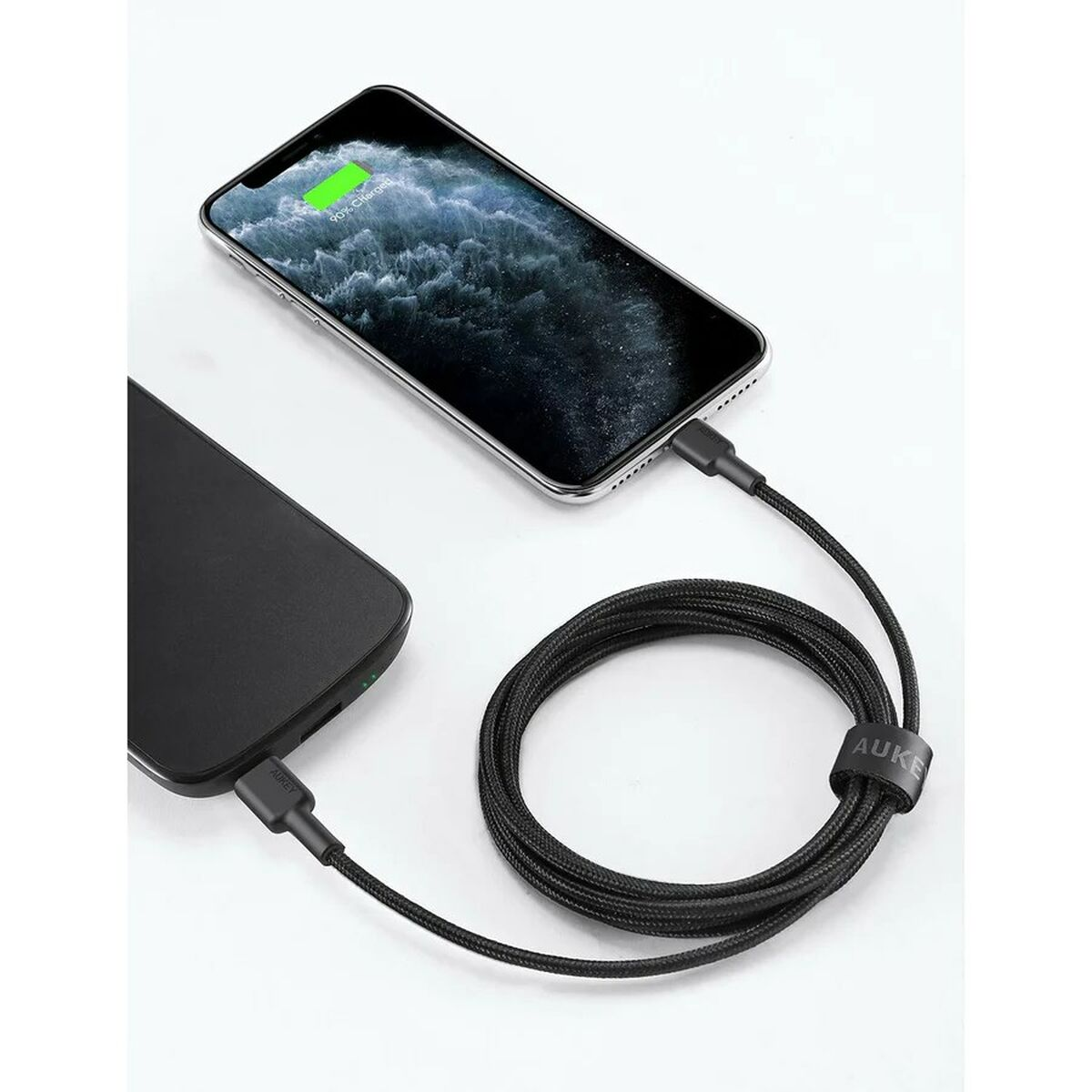 Un telefono nero si sta caricando con un cavo nero, collegato a un caricatore nero. Il telefono mostra il 90% di carica.