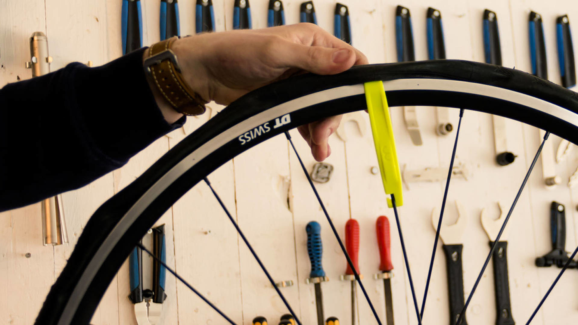 Osoba zdejmuje oponę z obręczy roweru za pomocą żółtych łyżek. Narzędzia wiszą na ścianie.