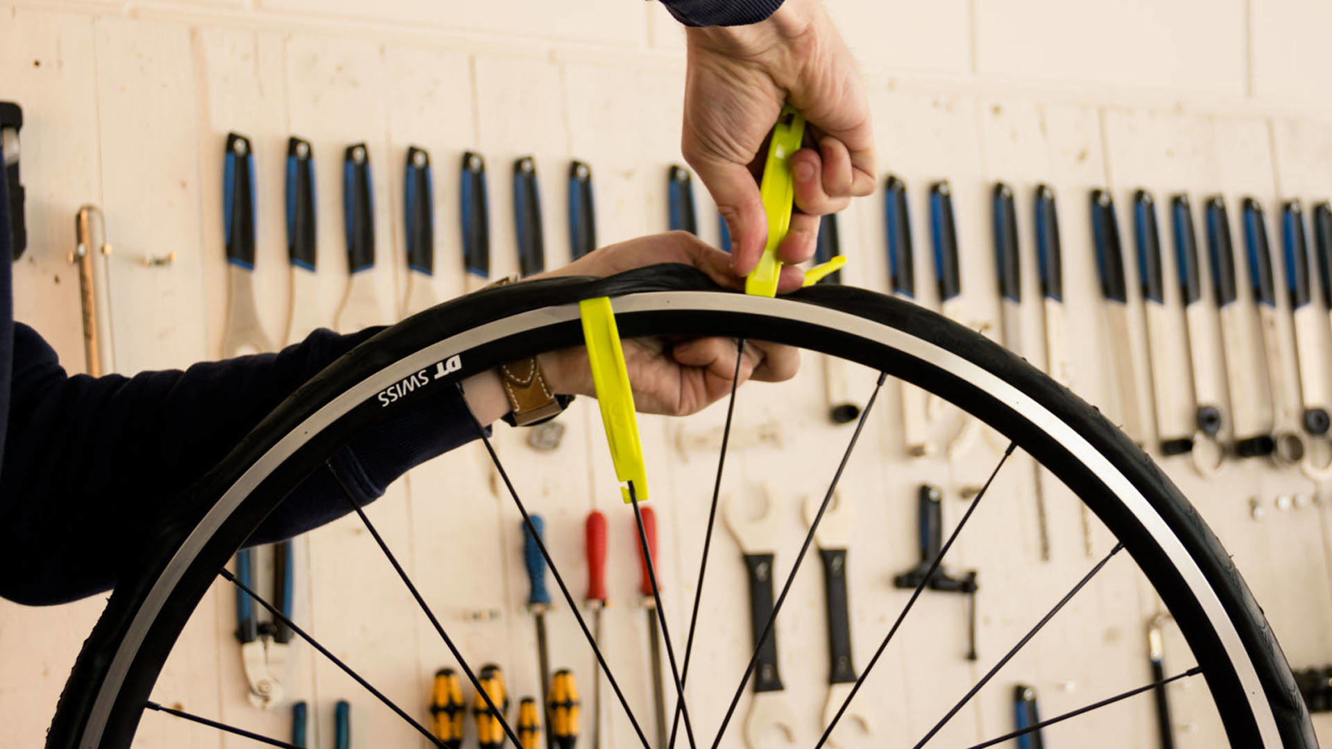 Osoba używa żółtych łyżek do opon, aby zdjąć oponę z obręczy roweru. Narzędzia na ścianie.