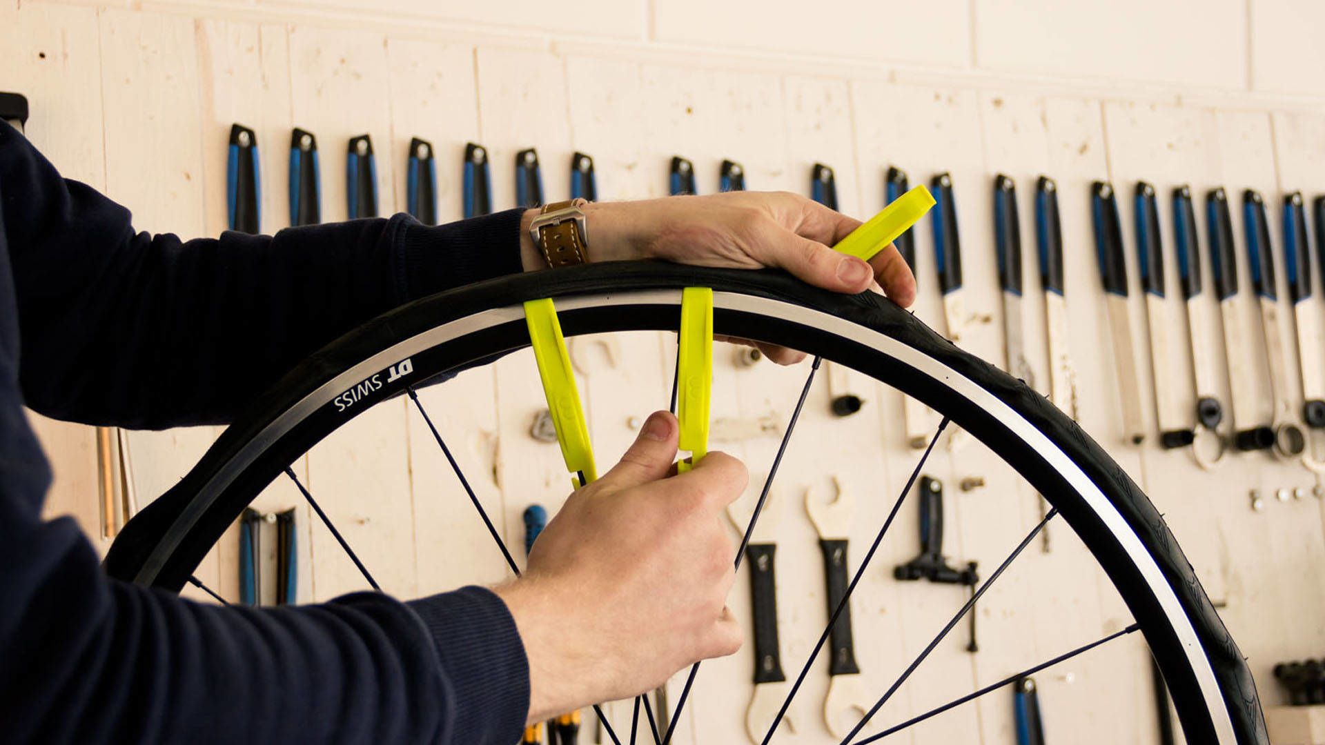 Ręce używające żółtych łyżek do opon do zdejmowania opony z koła roweru.