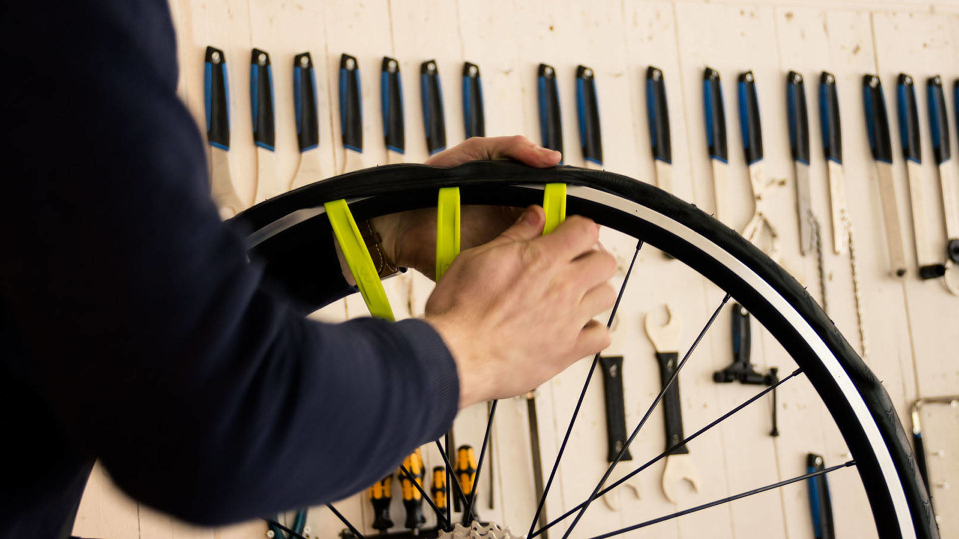 Ręce osoby używającej żółtych narzędzi do zdejmowania opony. Narzędzia wiszące w tle.