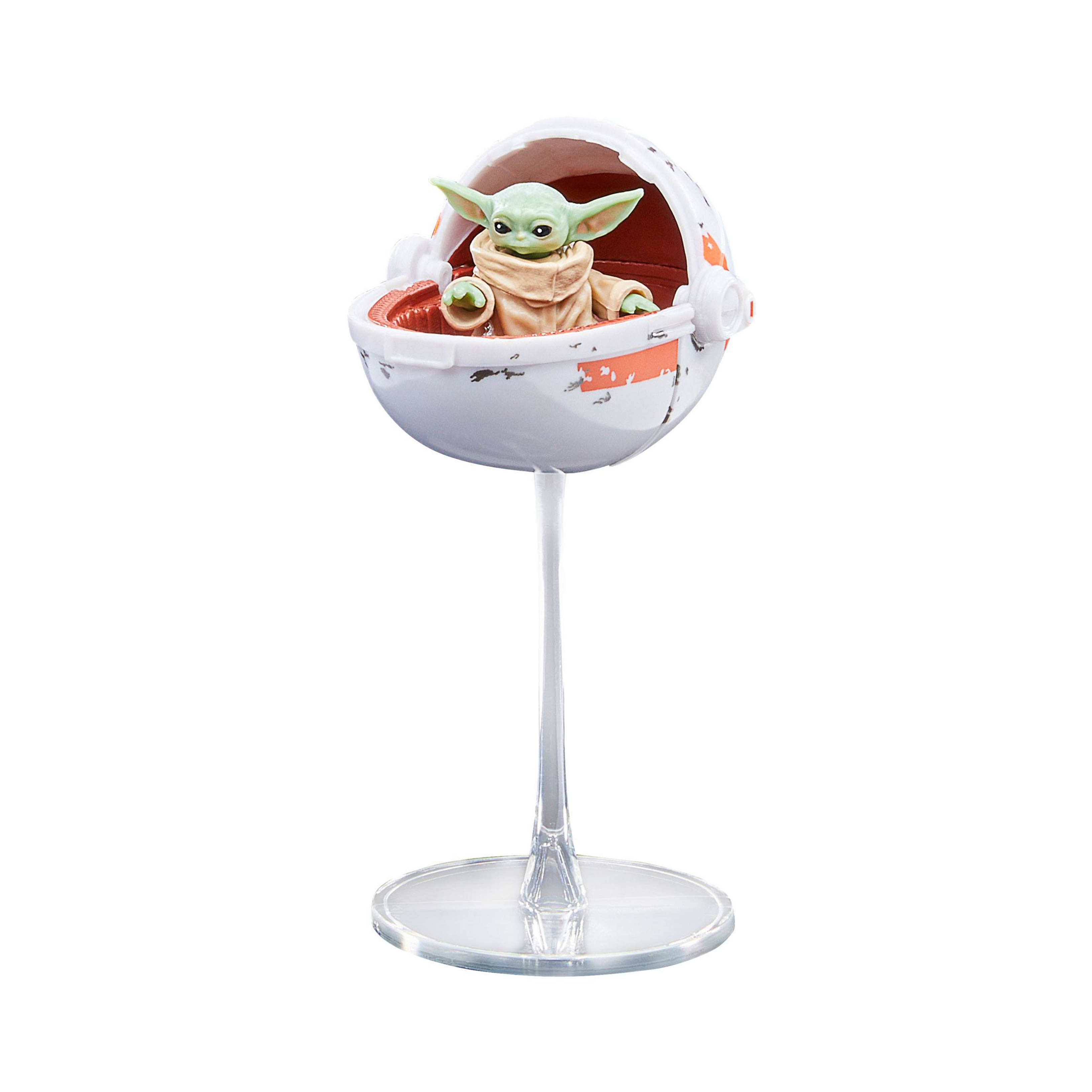 Beyaz bir kapsülde Baby Yoda figürü, şeffaf bir stand üzerinde. Beyaz zemin.