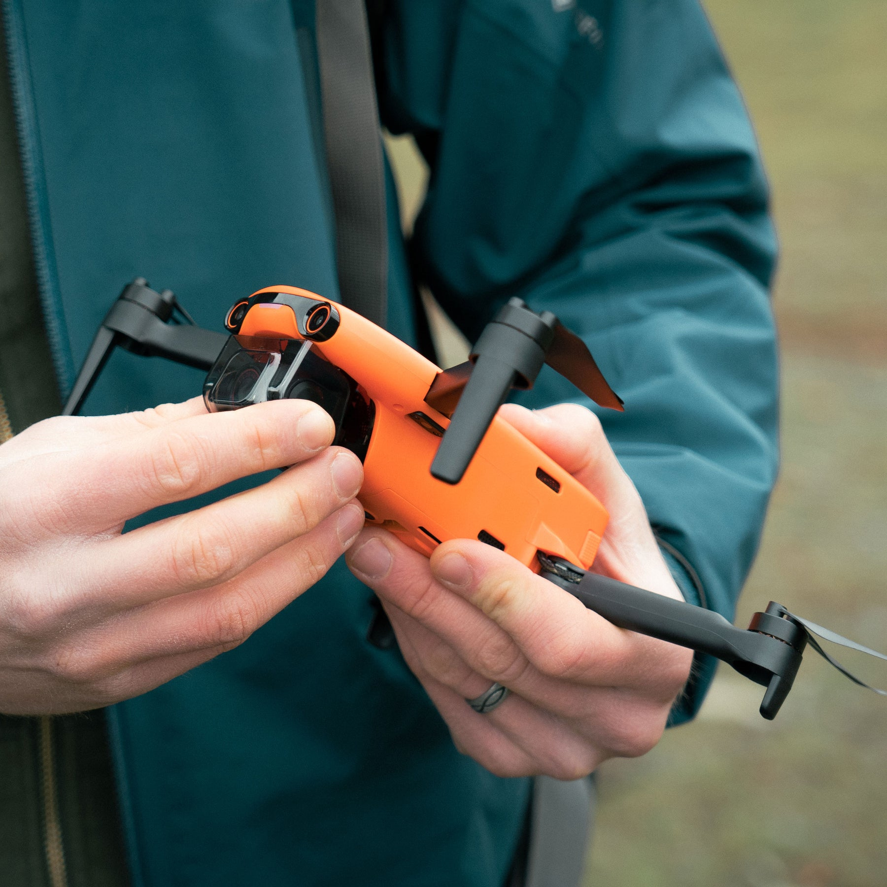 Una persona che tiene in mano un drone arancione, con eliche nere, all'aperto.