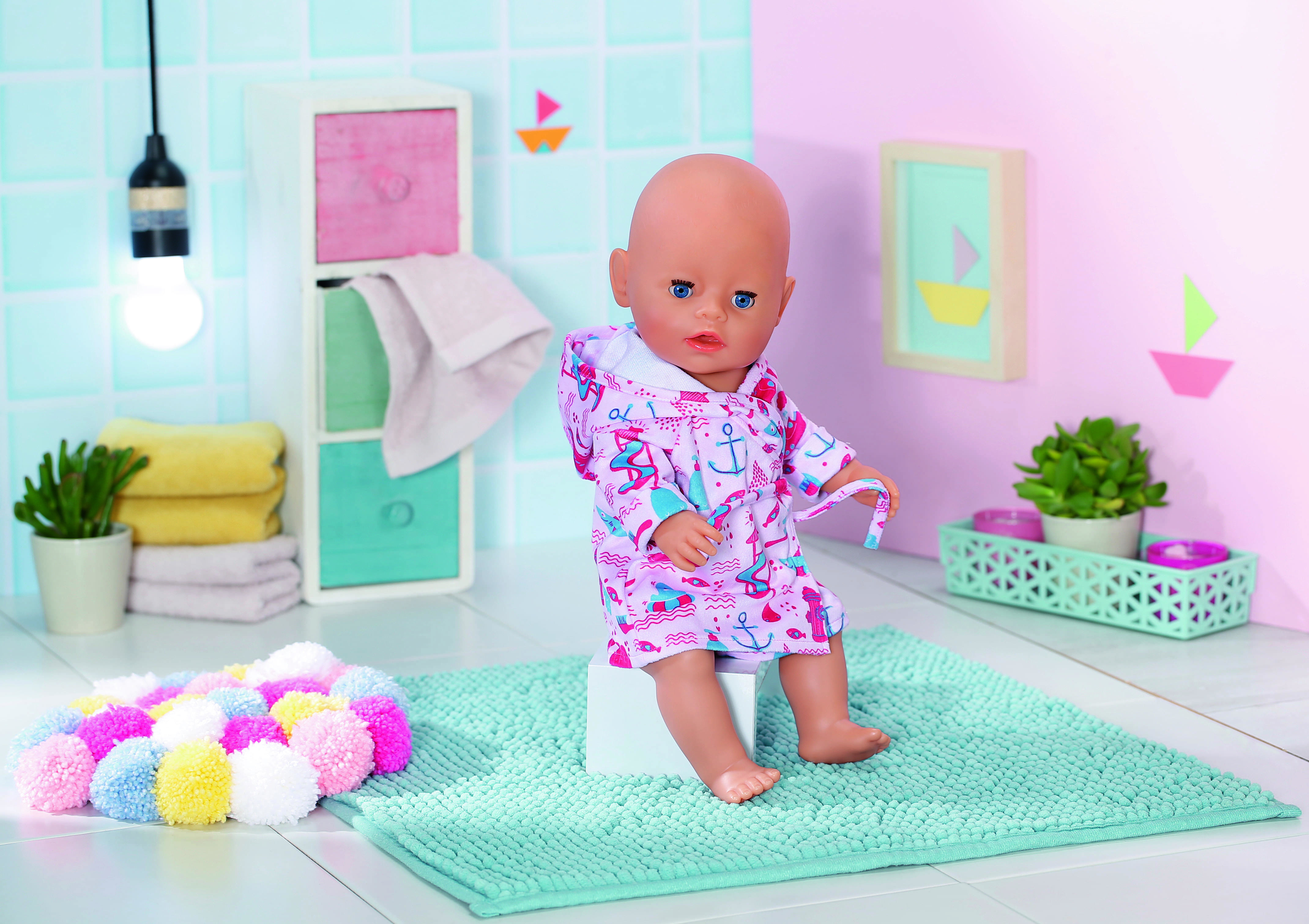 Lalka w otoczeniu łazienki. Ma na sobie szlafrok i siedzi na białym klocku.