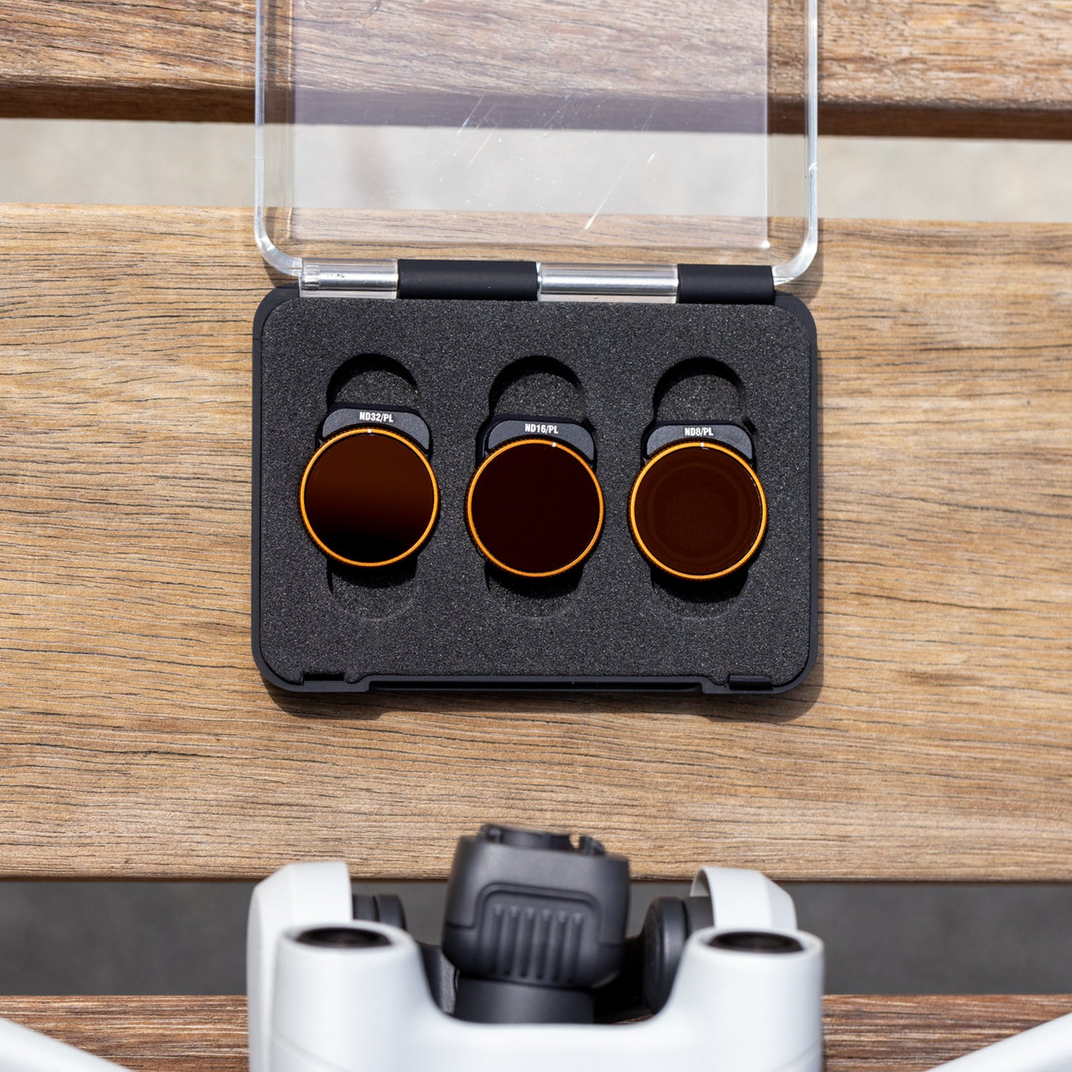 Drei Kameraobjektivfilter in einem schwarzen Gehäuse auf einer Holzoberfläche. Filter sind orange und schwarz.