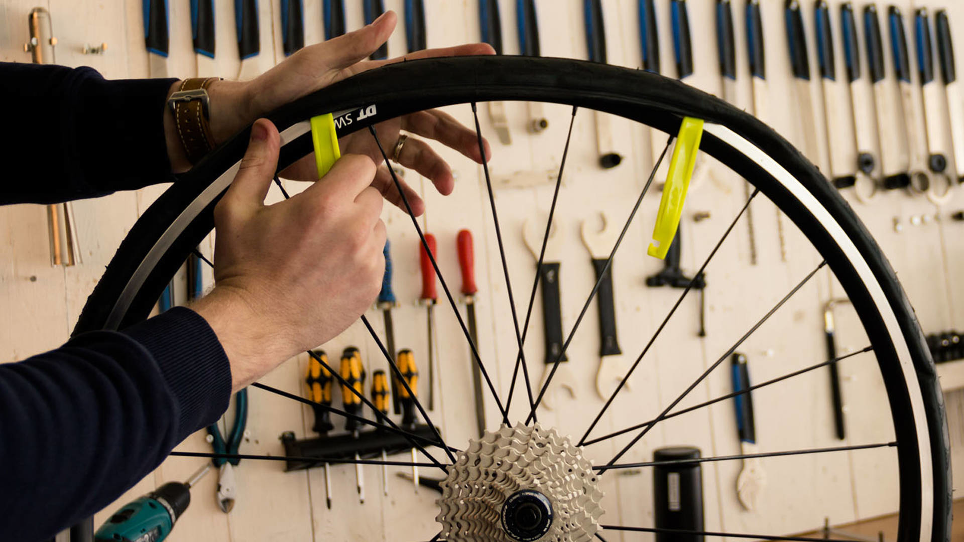 Osoba używająca żółtych łyżek do opon na kole roweru z narzędziami na ścianie.