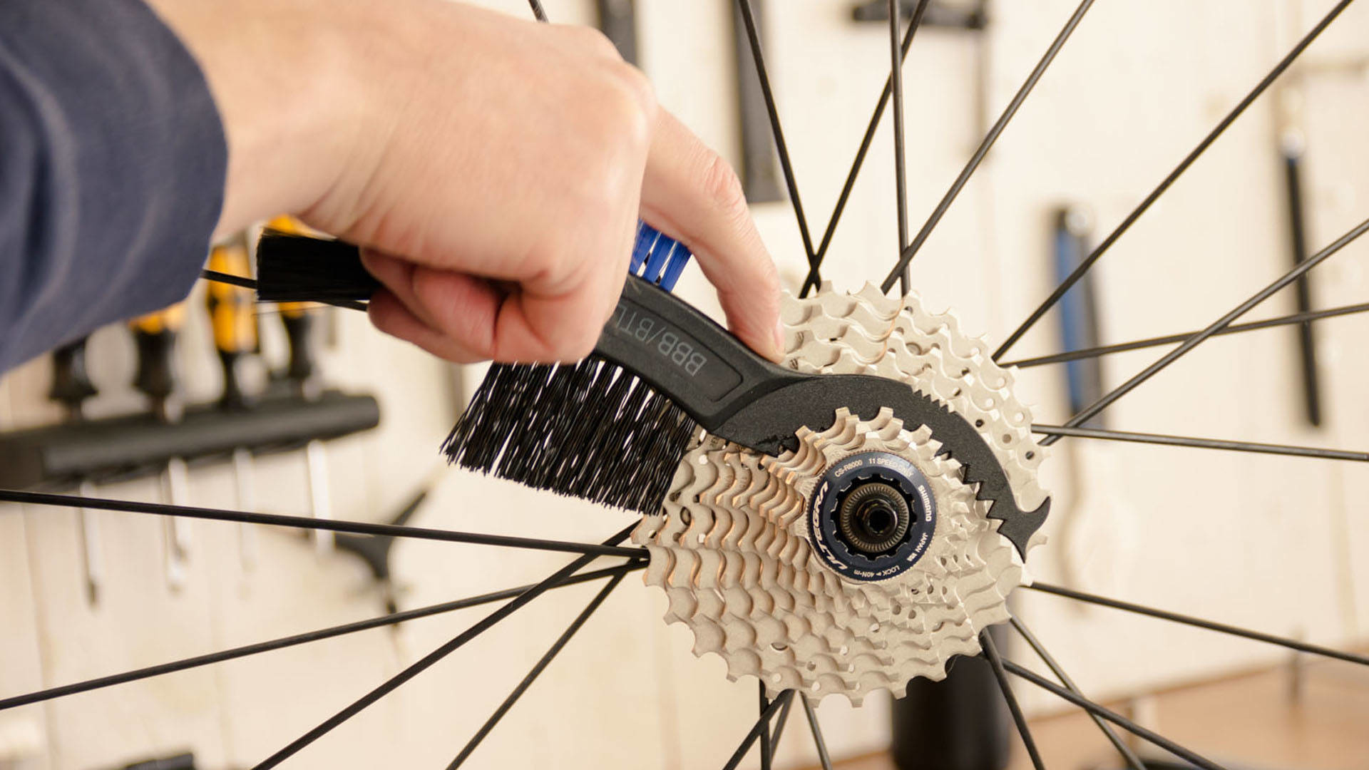 Ręka czyszcząca kasetę roweru szczotką. Koło roweru w tle. Ręka jest w centrum uwagi.