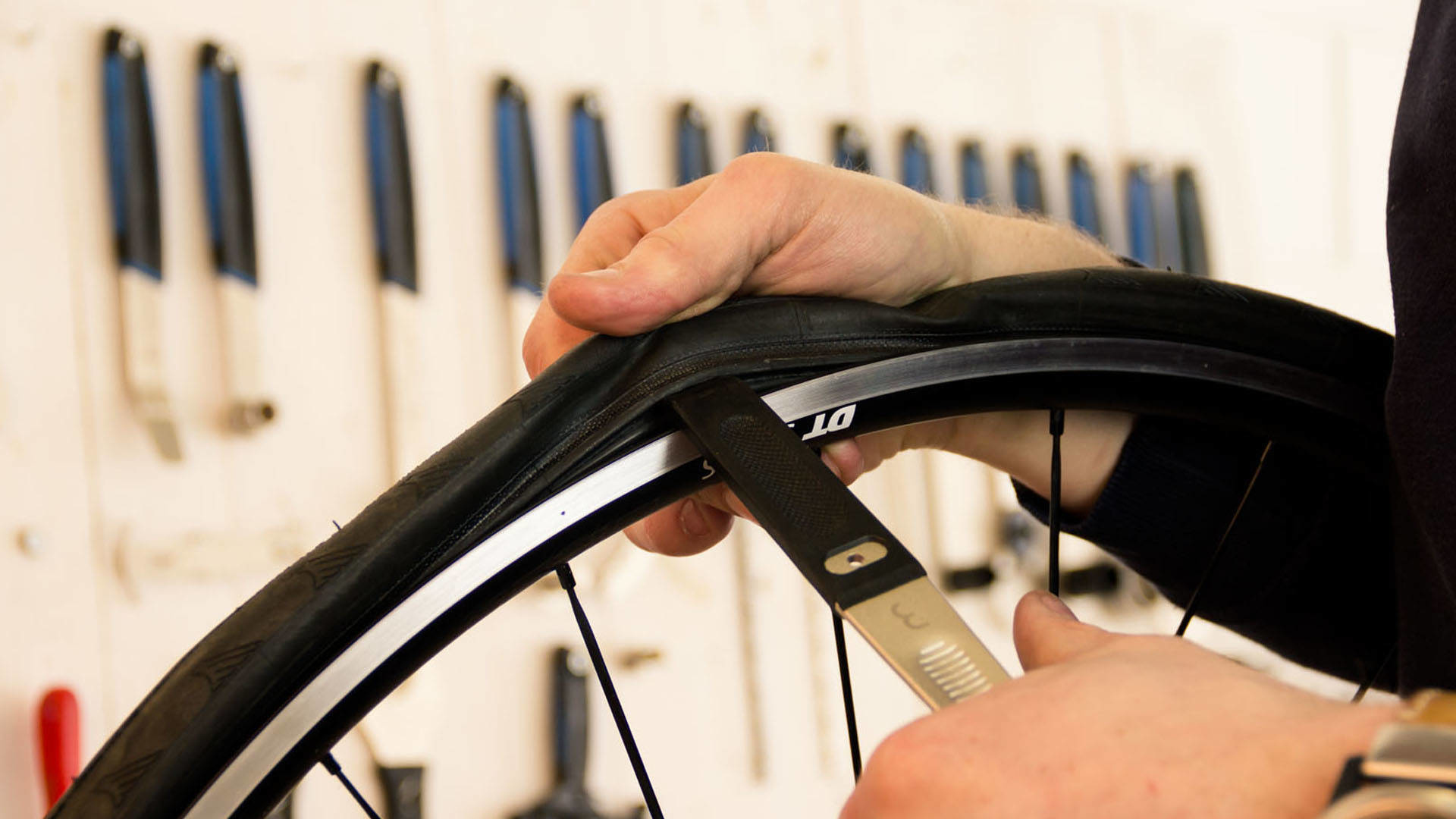 Ręce osoby używającej narzędzia do zdejmowania opony z koła roweru. Narzędzia w tle.