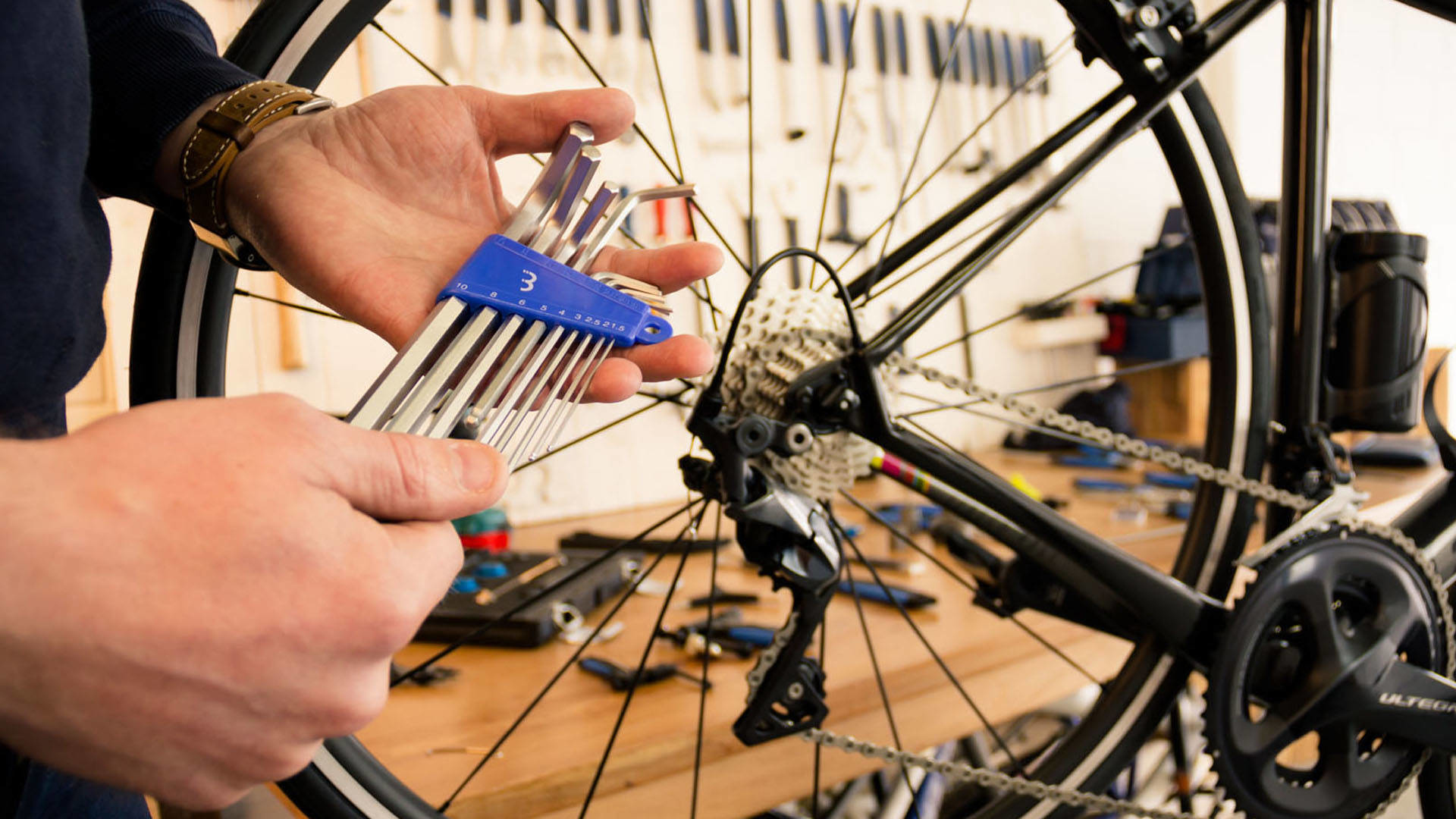 Osoba używająca kluczy imbusowych do pracy nad kołem roweru. Widoczne narzędzia i koło.