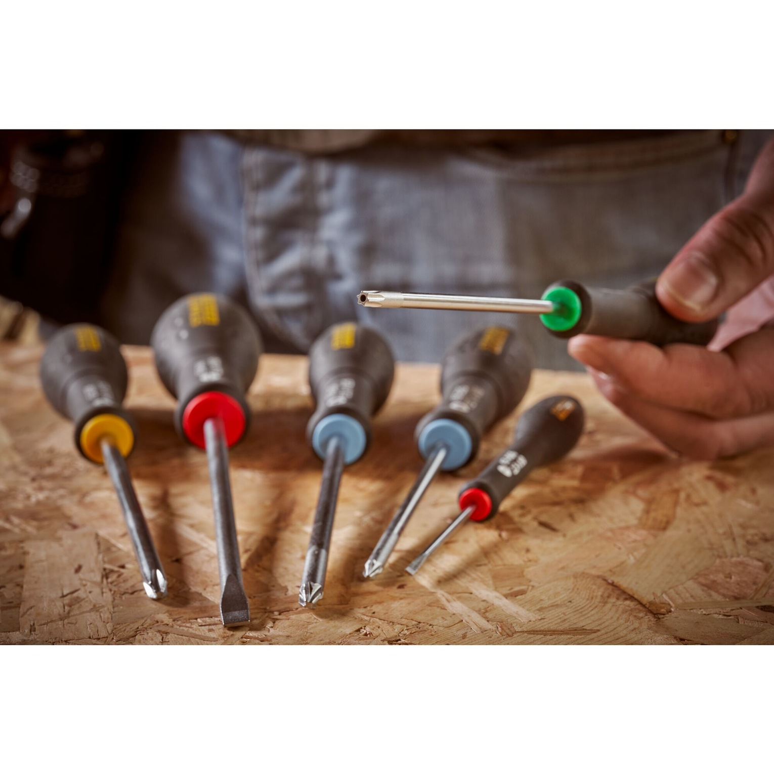 Śrubokręty na drewnie. Różne rozmiary, czerwone, żółte i niebieskie uchwyty. Niektóre ostre.