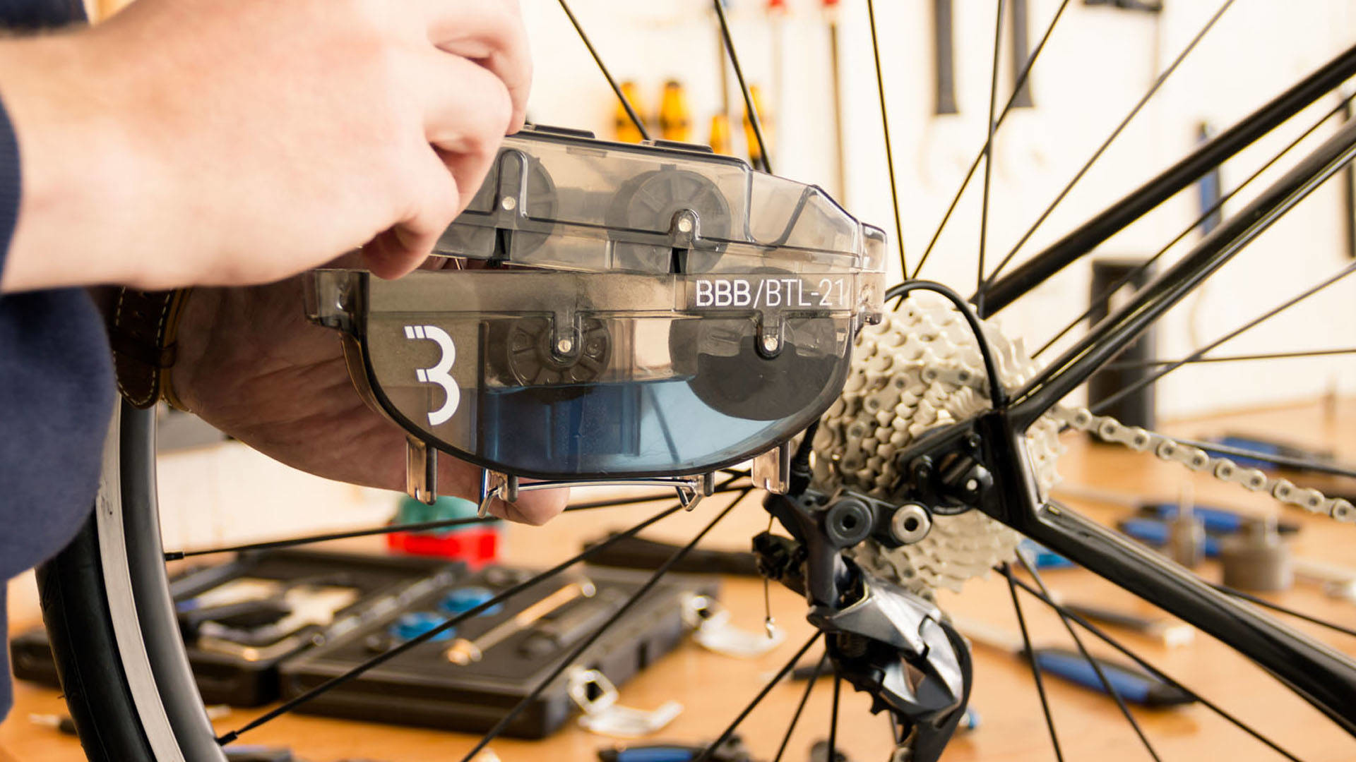 Osoba czyszcząca łańcuch rowerowy czarnym narzędziem czyszczącym na stole warsztatowym.