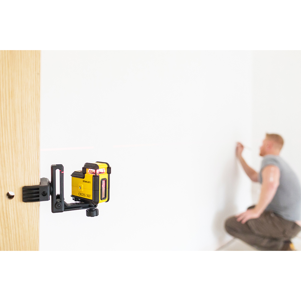 Poziomica laserowa zamontowana na ścianie. Mężczyzna w rozmytym tle, blisko ściany.