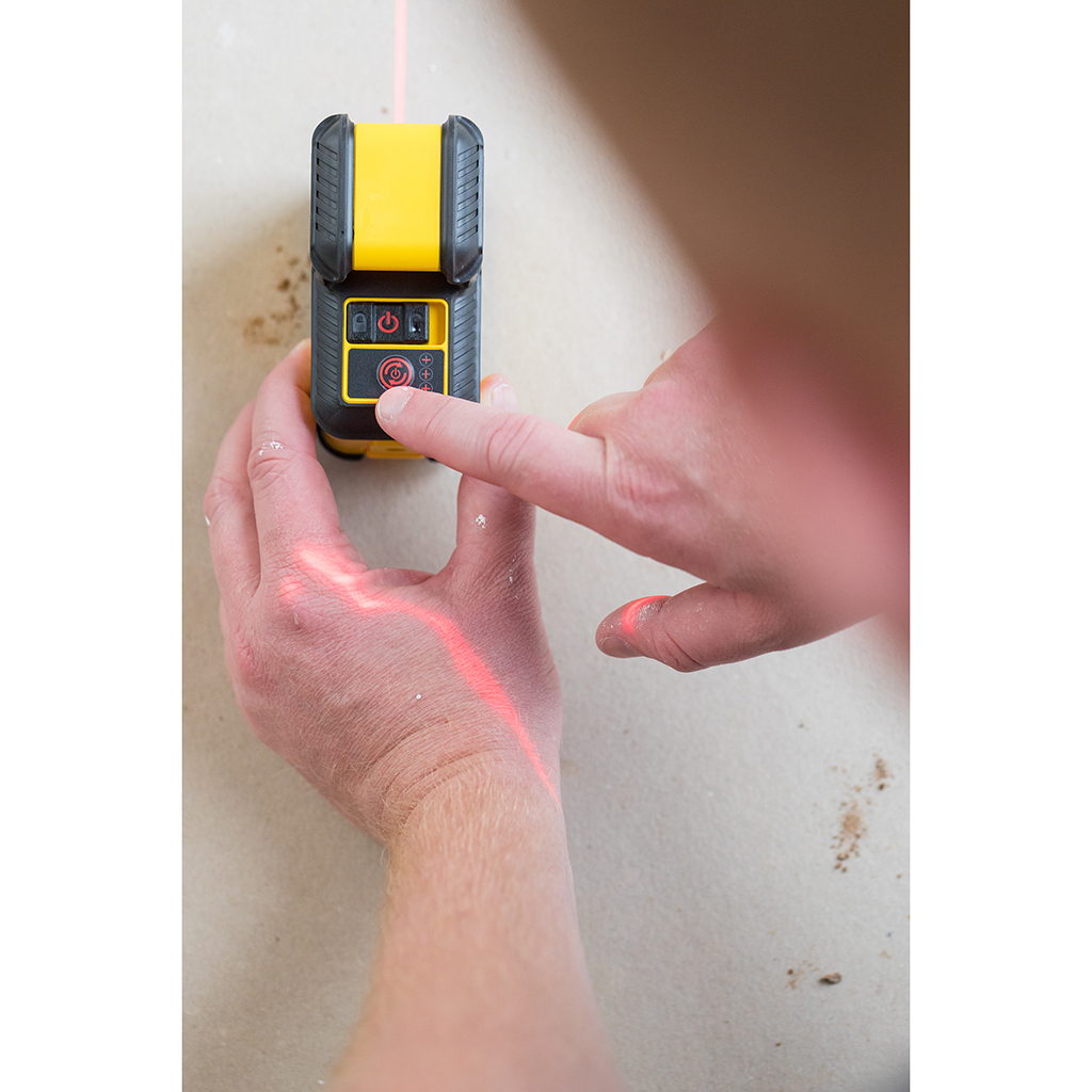 Dłonie używające żółto-czarnego poziomnicy laserowego na ścianie, widoczny czerwony laser.