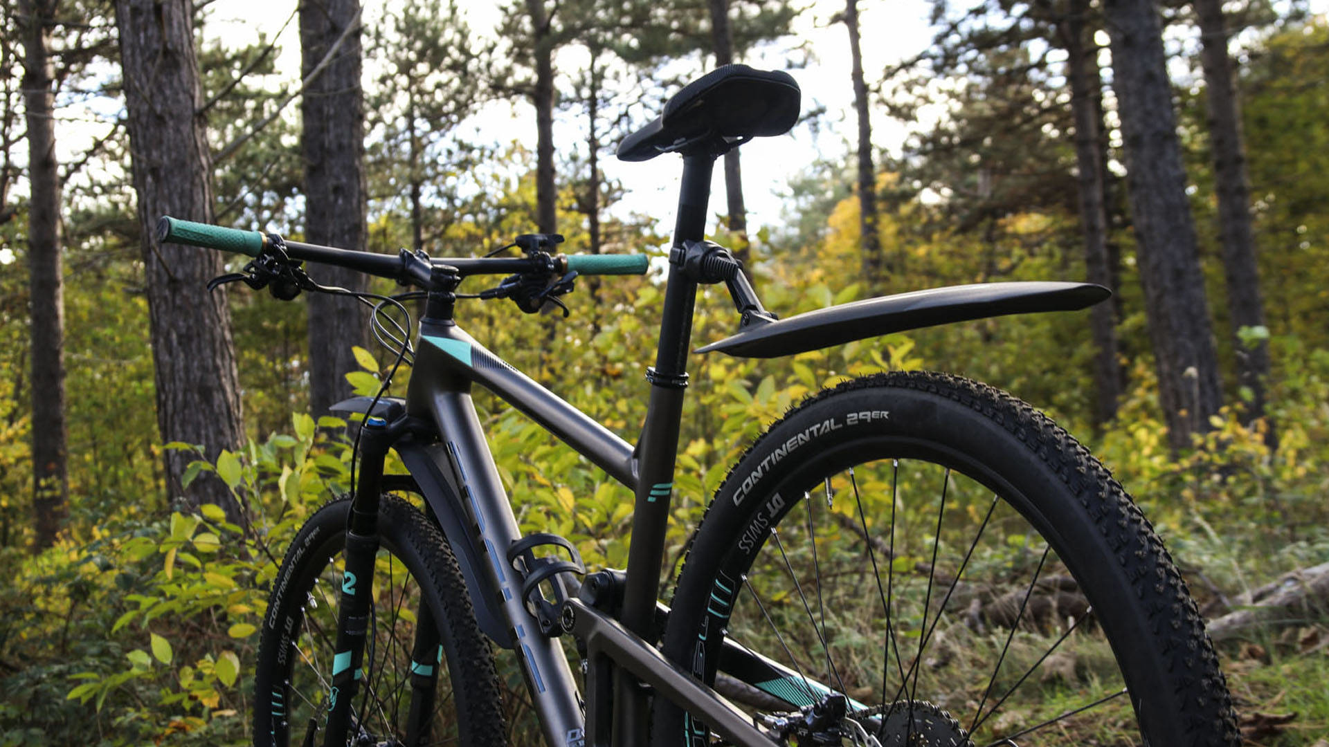 Rower górski w leśnym otoczeniu, z zieloną kierownicą i czarnym błotnikiem.